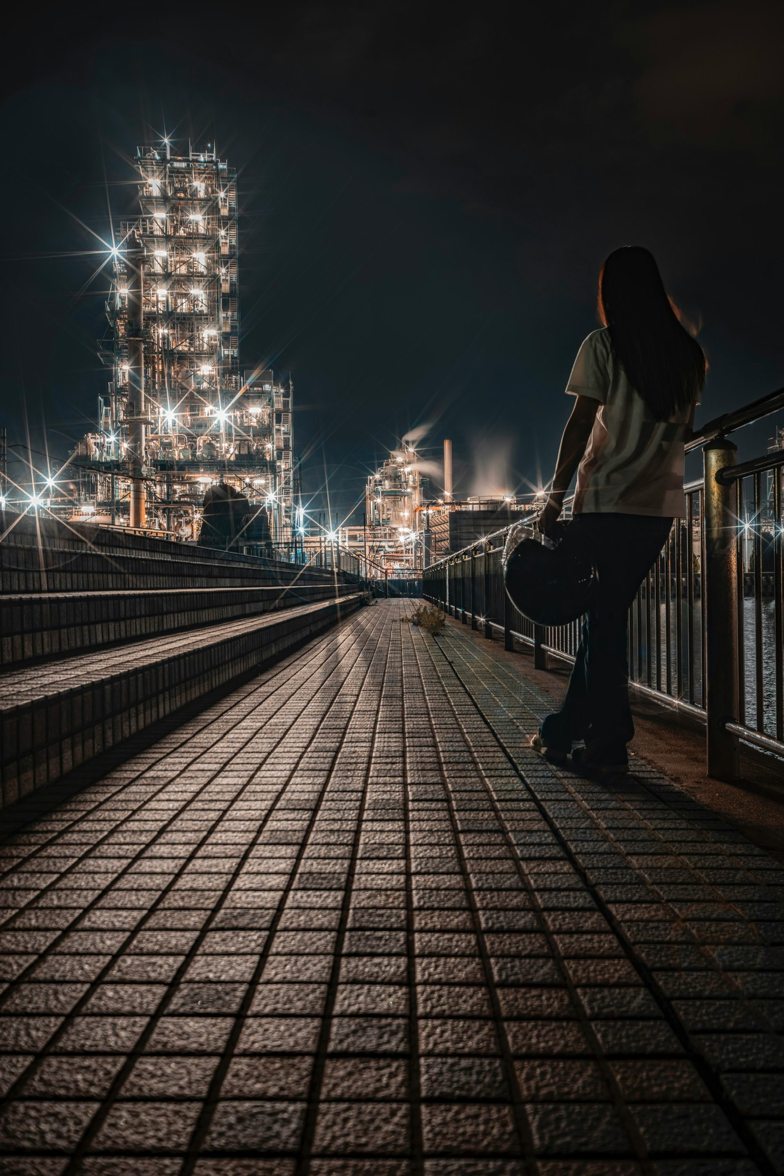 Eine Person hält eine Gitarre auf einem Industrie-Weg bei Nacht