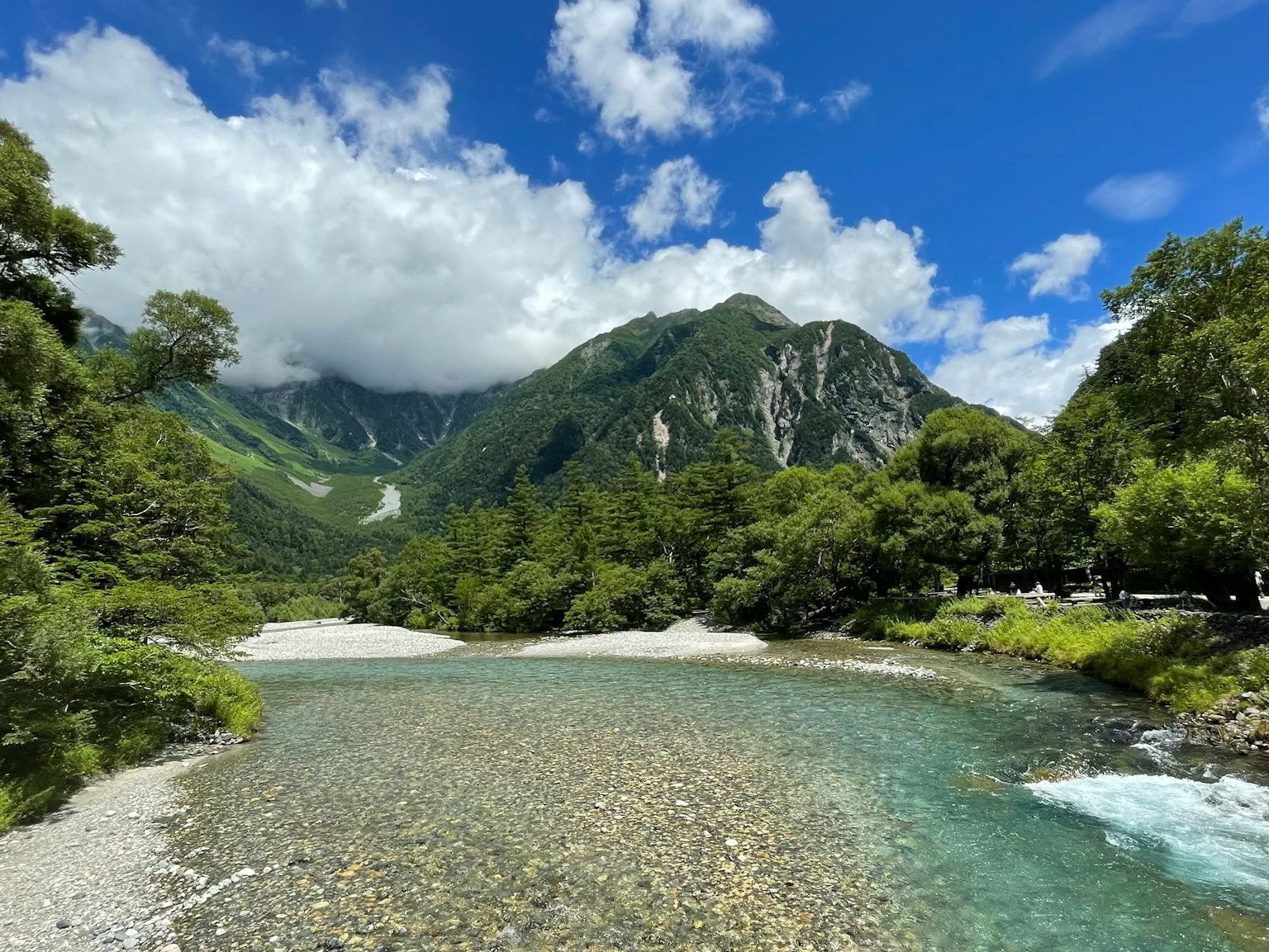 Malersicher Blick auf einen klaren Fluss, der unter üppigen grünen Bergen und einem blauen Himmel fließt