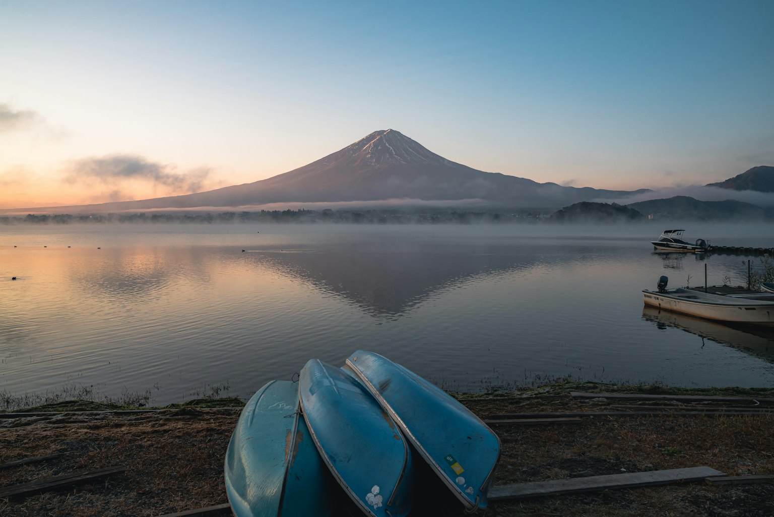 Mont Fuji reflété sur un lac calme avec des bateaux bleus au premier plan