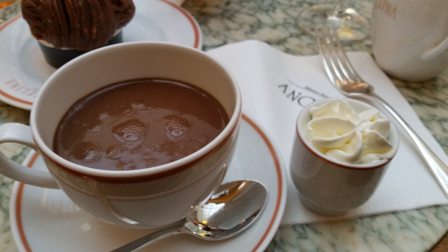 A cup of warm chocolate with a side of whipped cream on a marble table