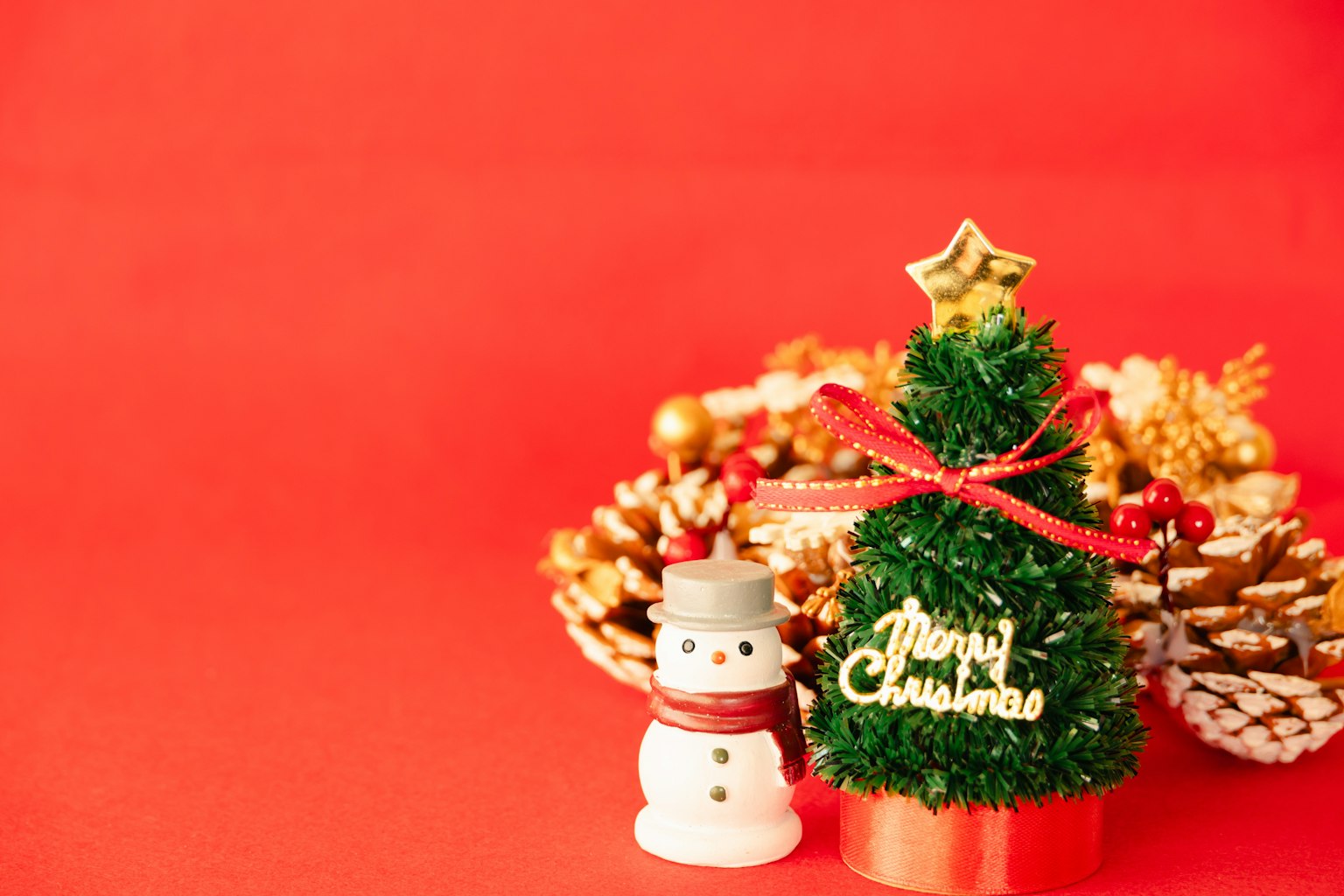 Ein kleiner Weihnachtsbaum und eine Schneemann-Dekoration auf rotem Hintergrund