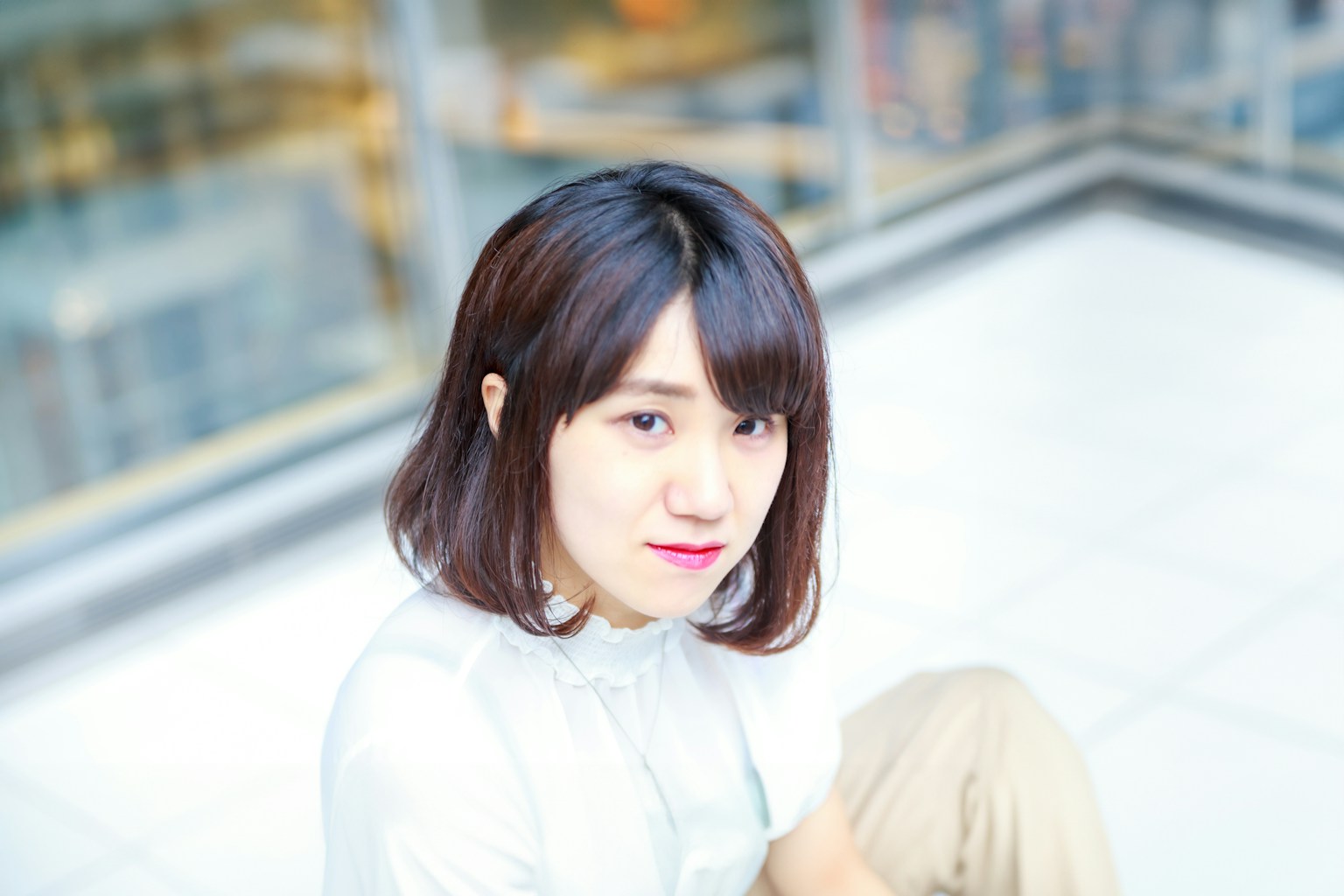 ภาพถ่ายหญิงสาวยิ้มบนพื้นหลังสว่างพร้อมผมยาวถึงไหล่สวมเสื้อสีขาว