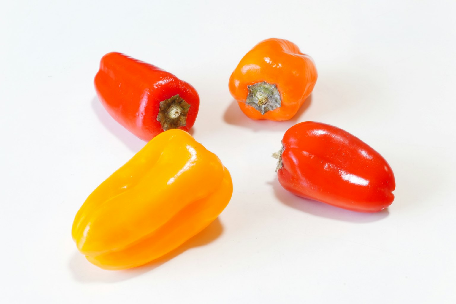 Poivrons colorés rouges, oranges et jaunes disposés sur un fond blanc