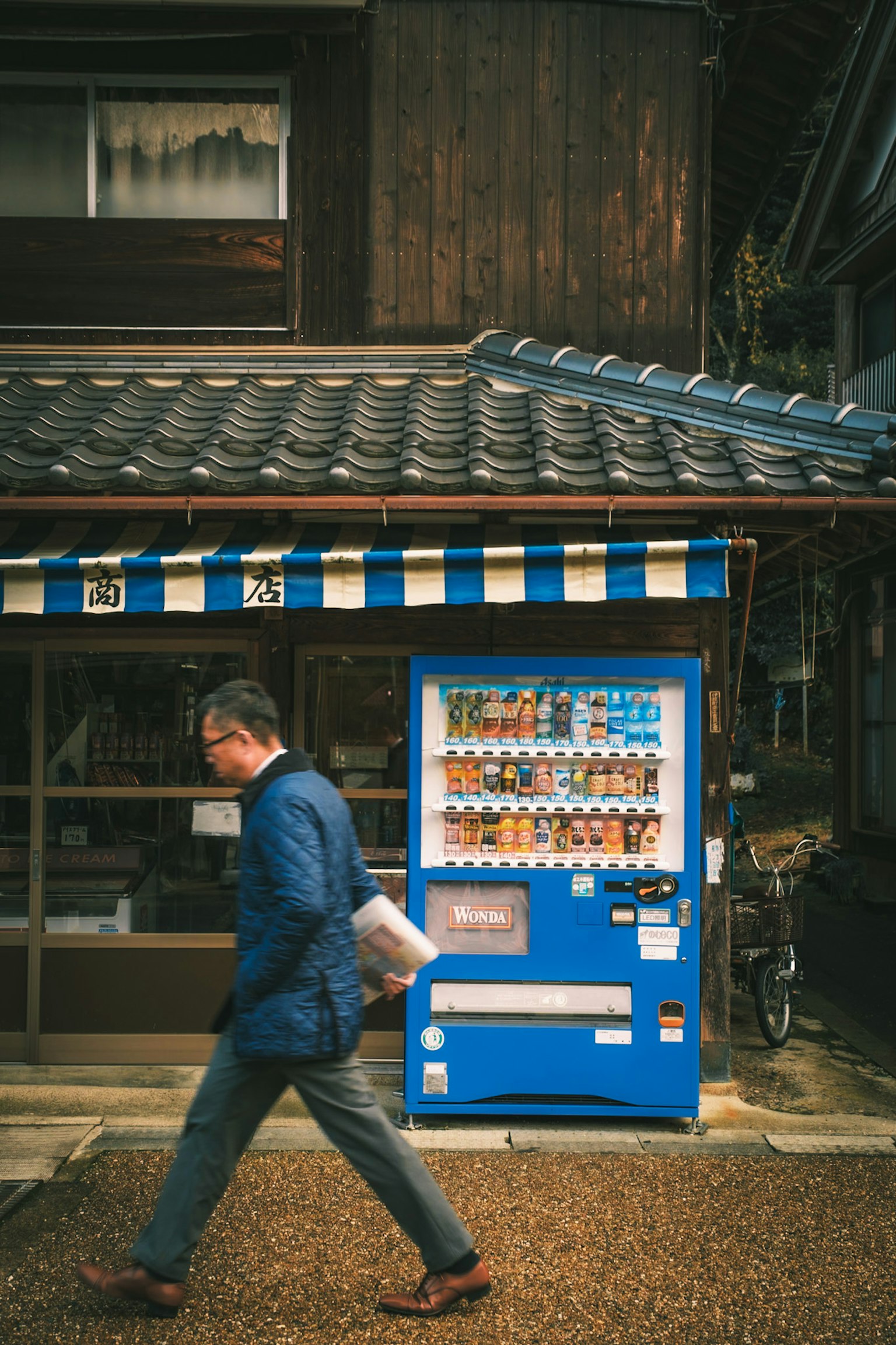 一名男子走過一台藍色自動販賣機，背景是一座傳統的日本建築