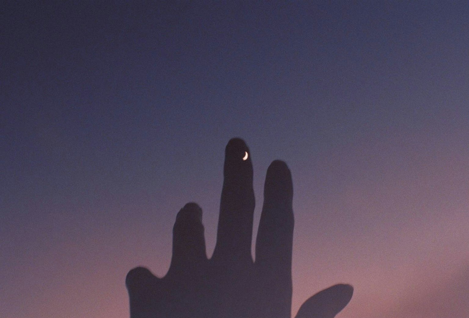 Silhouette einer Hand, die nach einem kleinen Halbmond in der Dämmerung greift