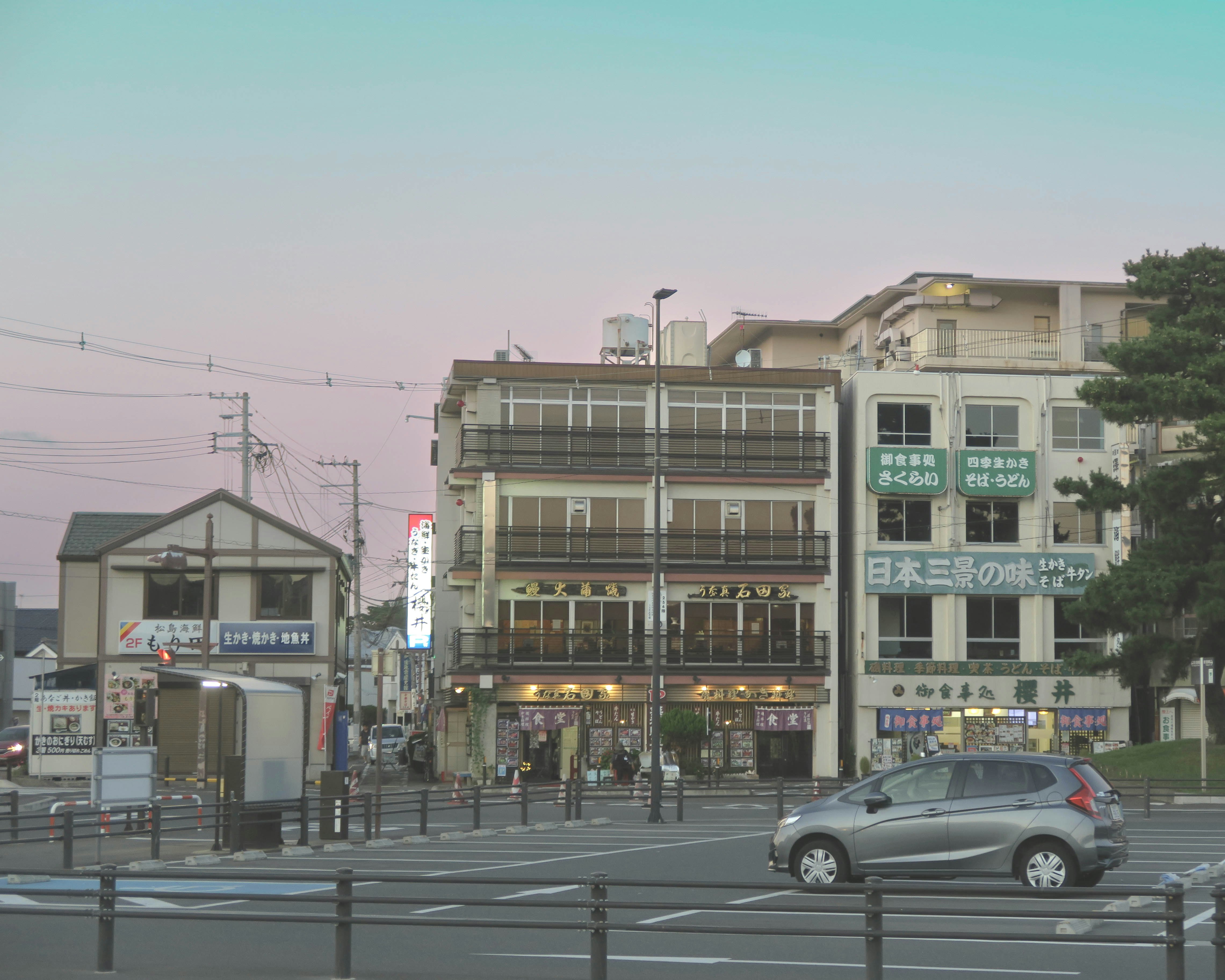 日本の街角の交差点で走る車と商店の看板が並ぶ風景