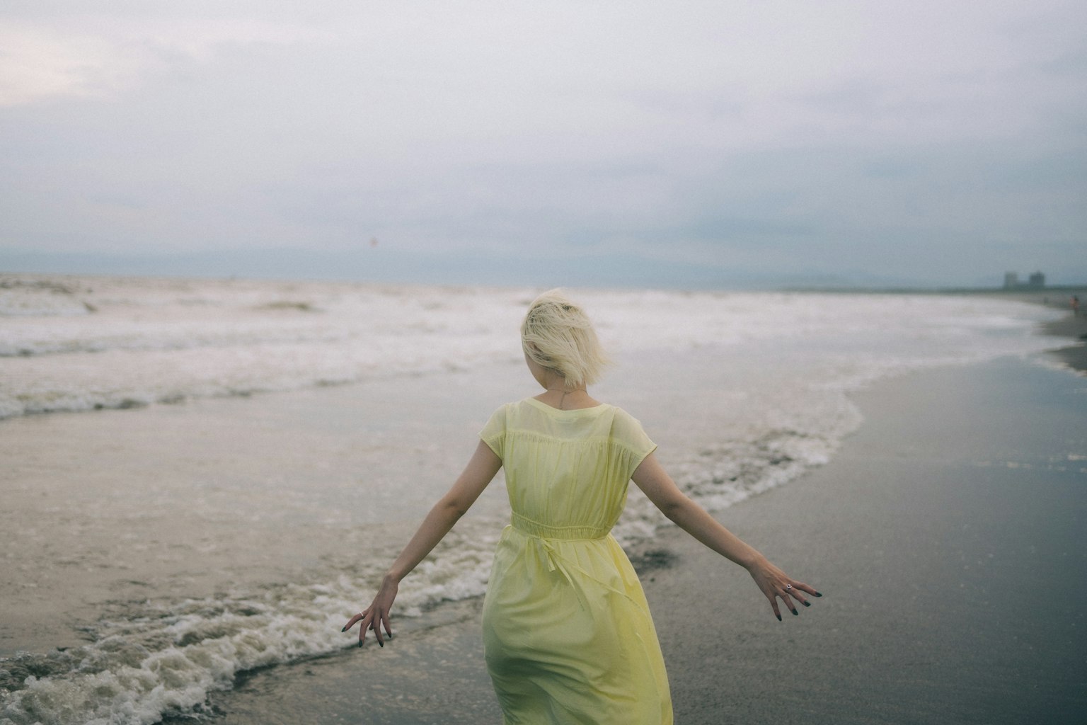 Una donna in un vestito giallo in piedi sulla spiaggia di spalle