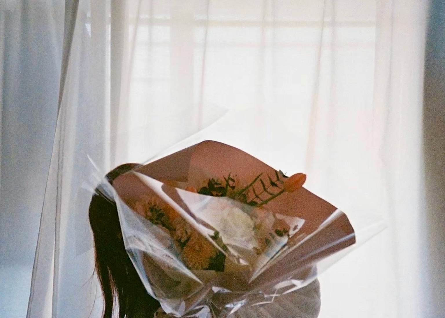 透明なカーテンの後ろにいる女性が花束を持っている