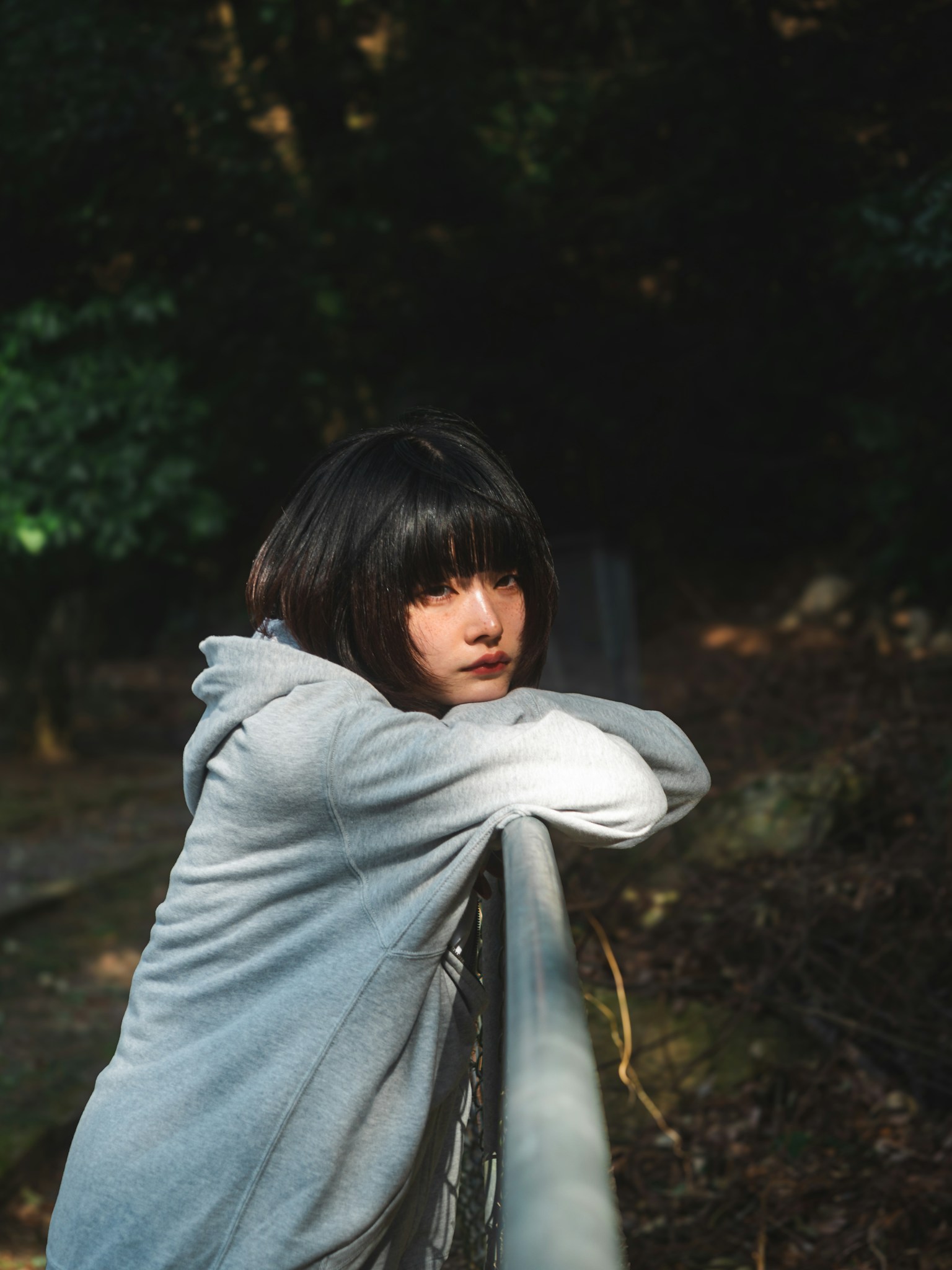 Portrait of a woman leaning on a park fence wearing a gray hoodie lost in thought in soft lighting