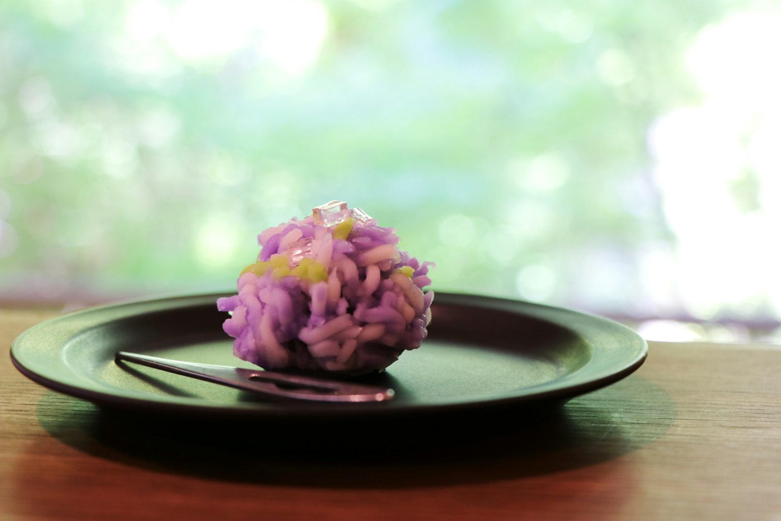 Un dessert a forma di fiore viola su un piatto nero con un cucchiaio d'argento