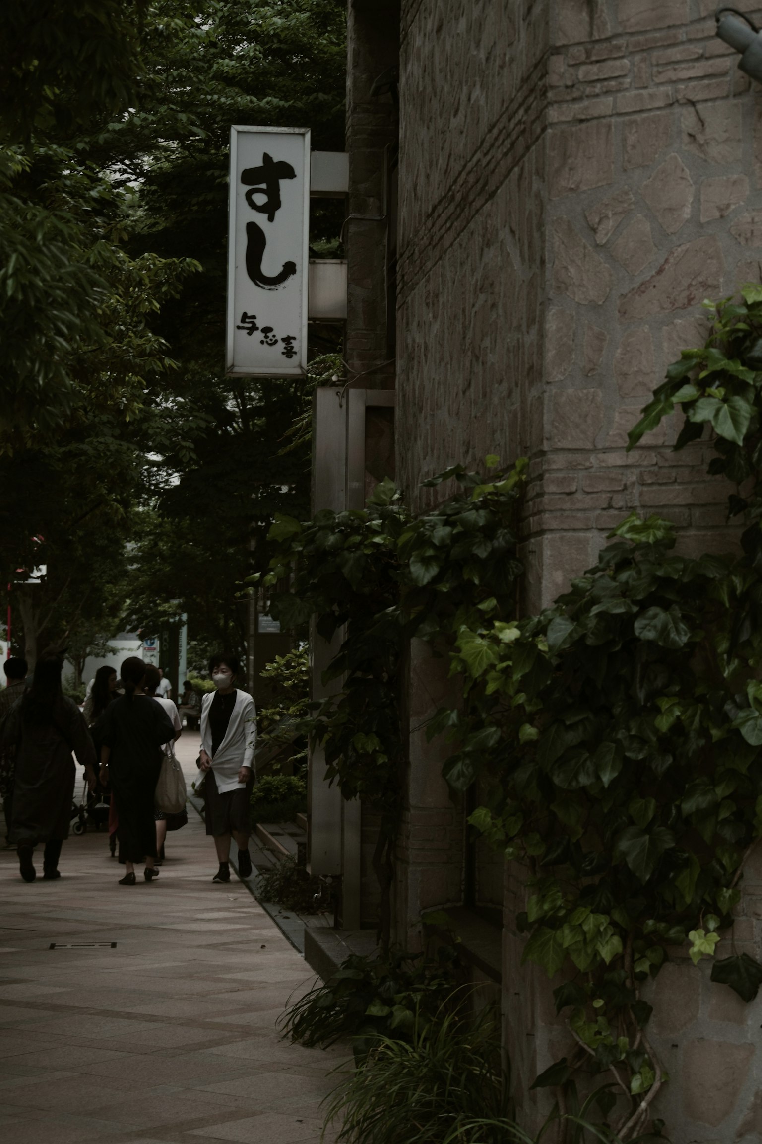 Sushi restaurant sign surrounded by greenery with pedestrians
