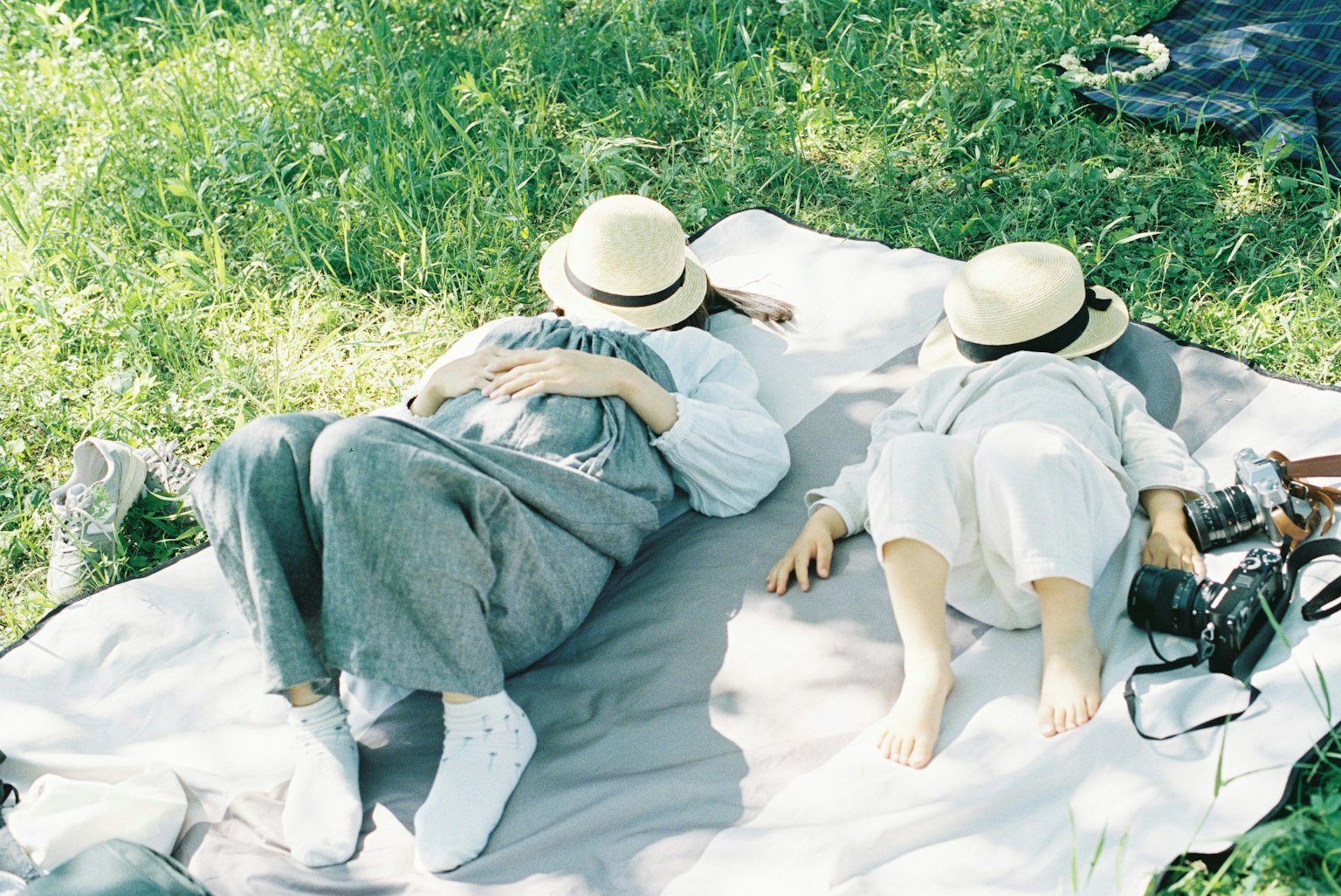 Hai người nằm trên thảm picnic trên cỏ xanh đội mũ trắng