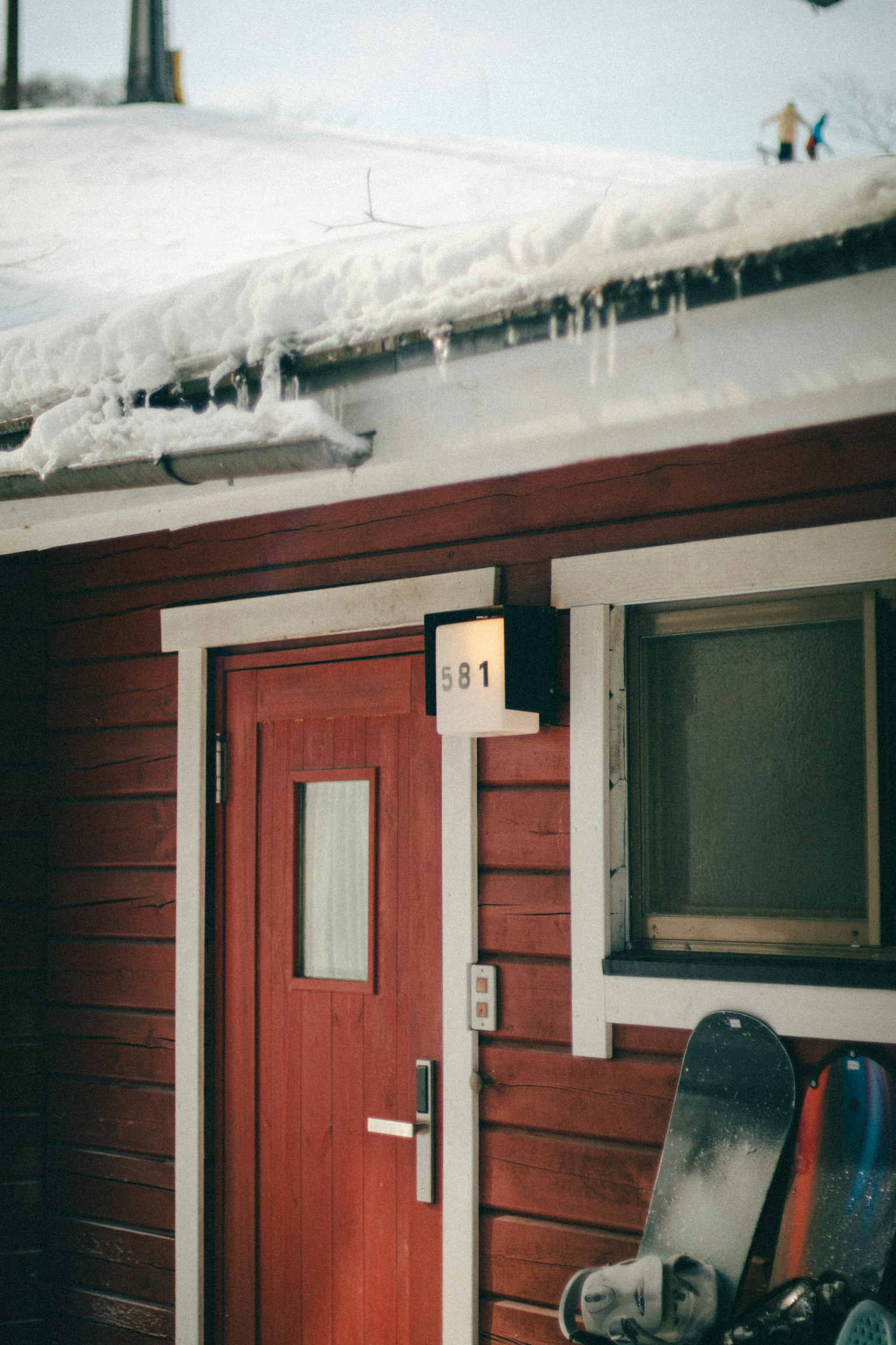 Porta e finestra di una casa rossa in un giorno nevoso Tetto coperto di neve e snowboard