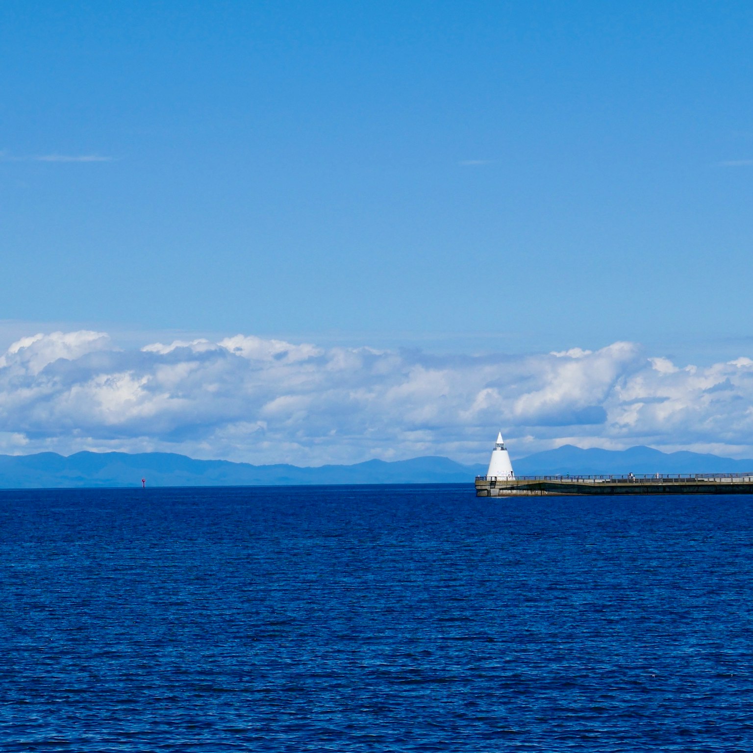 Un faro che si erge su un molo con un oceano e un cielo blu
