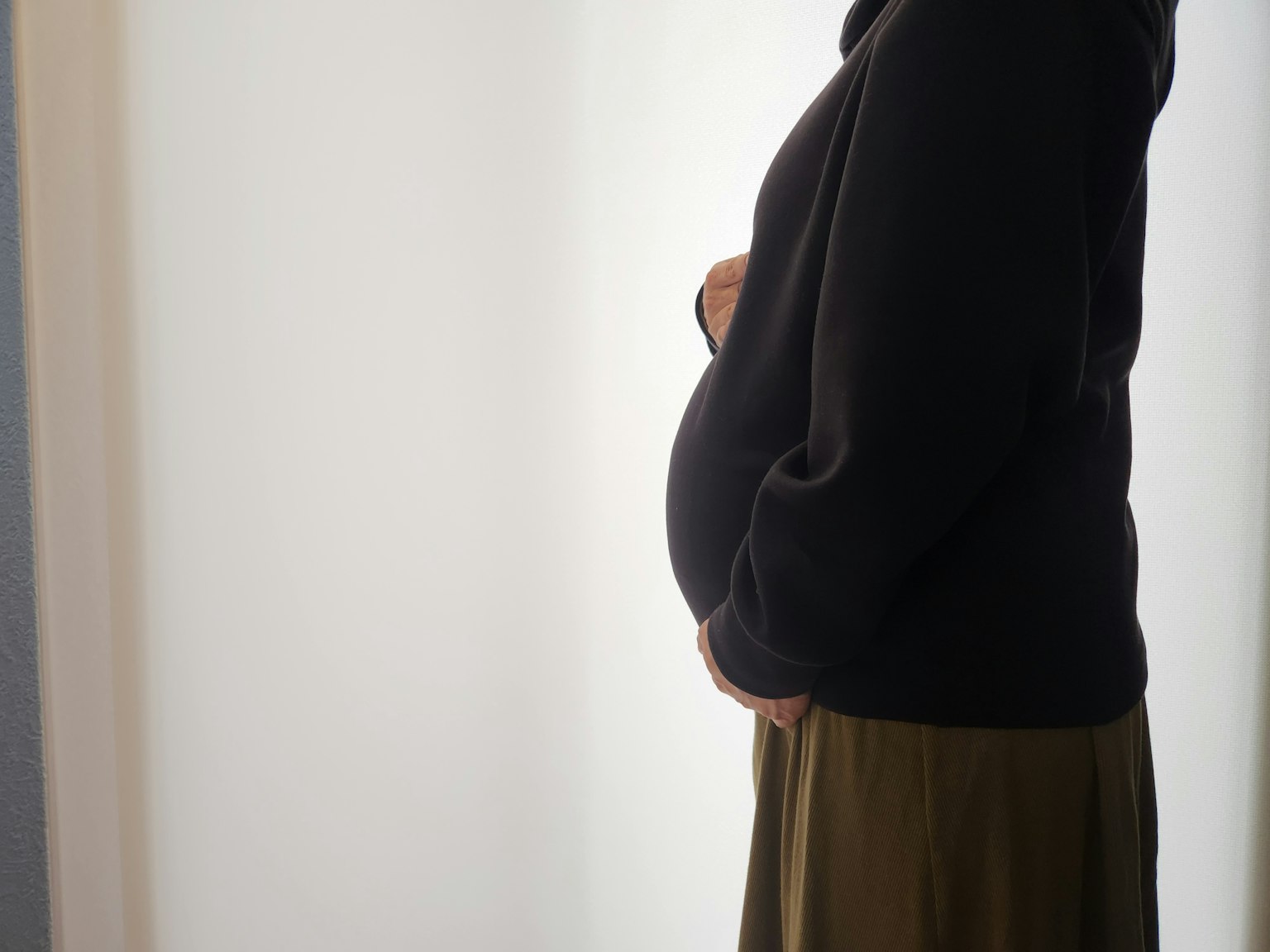 Pregnant woman standing in profile with hands on her belly