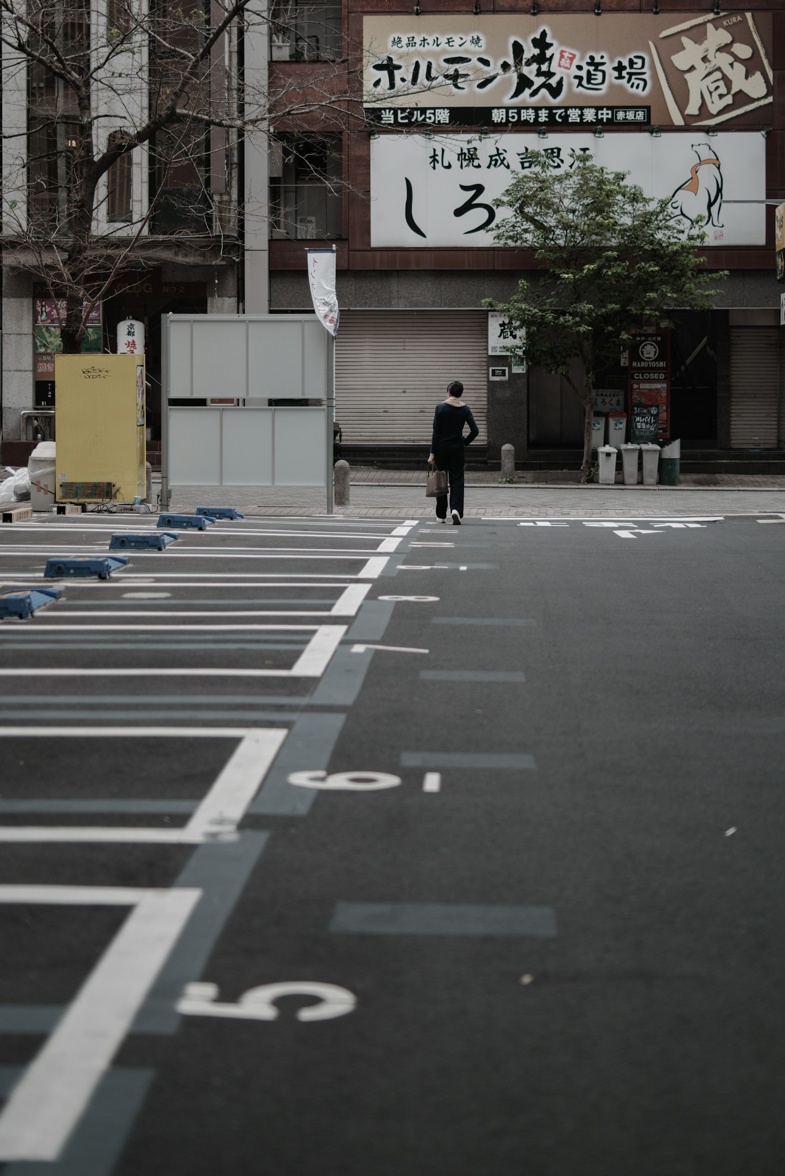 A person walking in an empty parking lot with a commercial building sign in the background