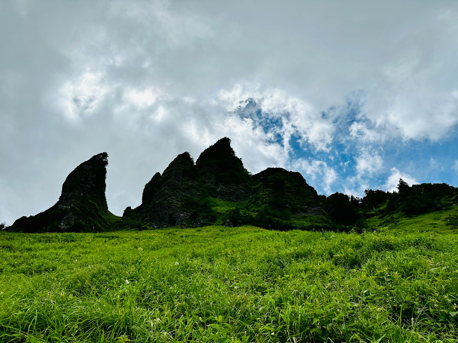 Silhouette of rocky peaks against a cloudy sky over green grass