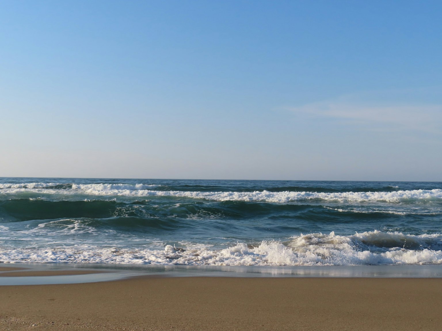 Strandszene mit blauem Himmel und brechenden Wellen