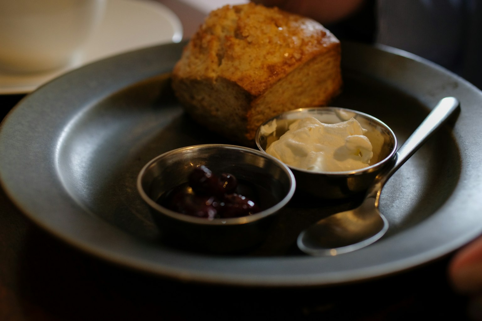 Un scone en un plato con dos pequeños cuencos de crema y bayas