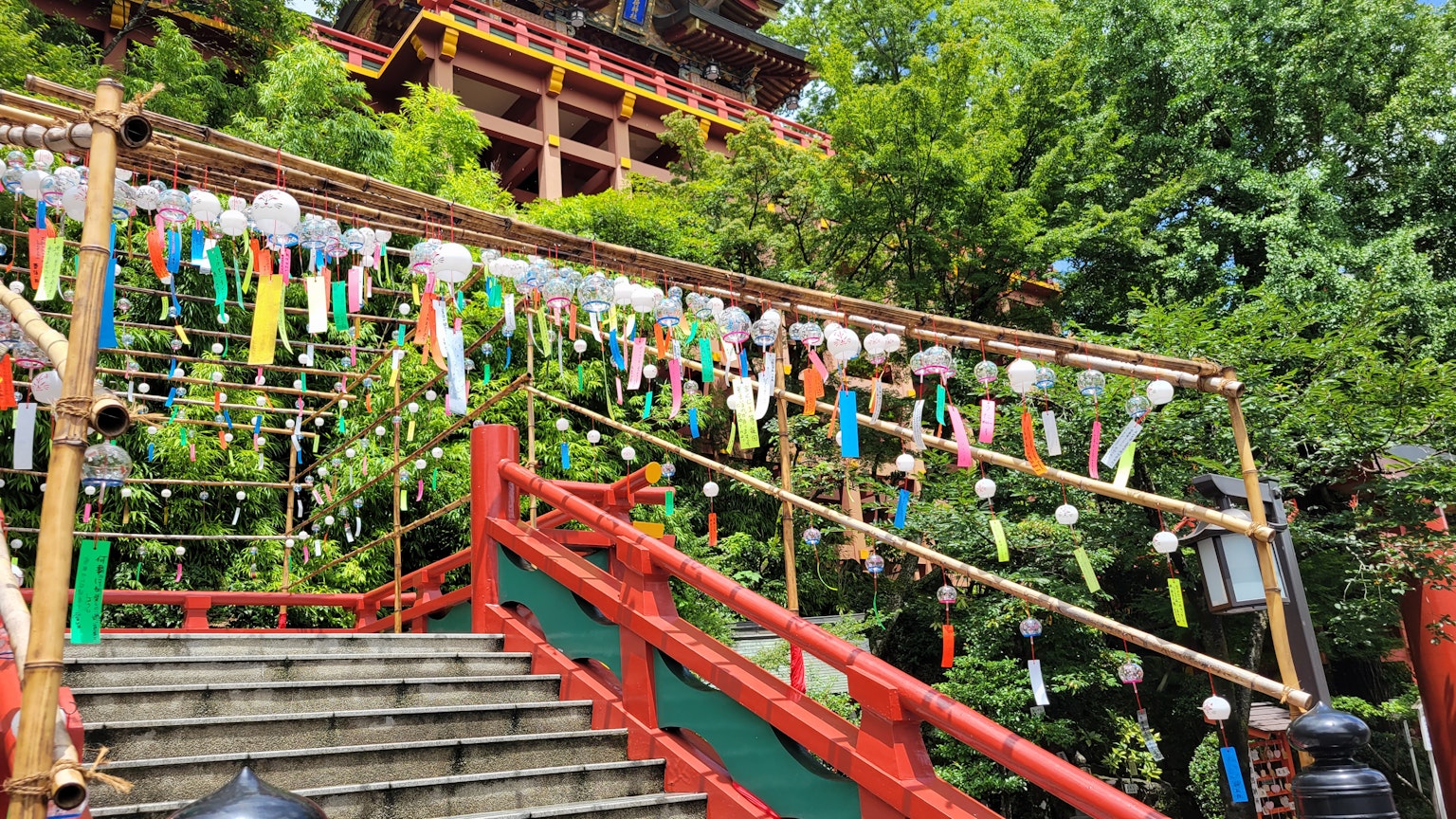竹製樓梯上懸掛風鈴的風景，紅色欄杆和郁郁蔥蔥的綠樹