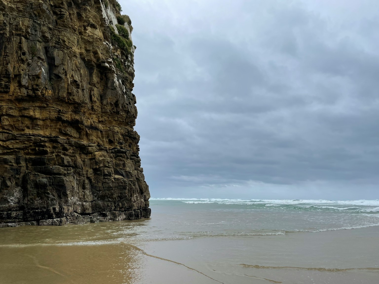 Acantilado rocoso junto a la playa bajo un cielo nublado