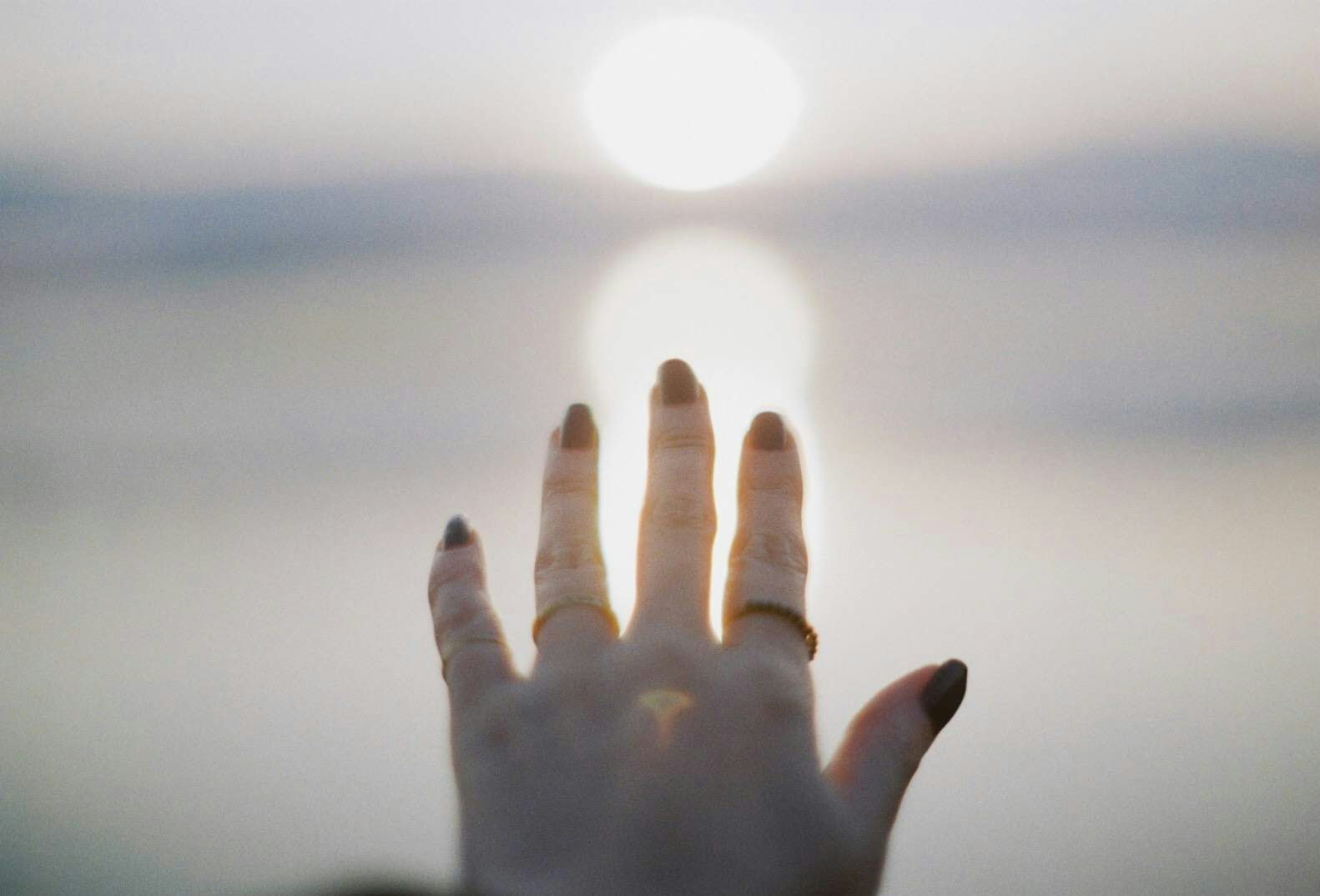 hand reaching toward the sun in backlight