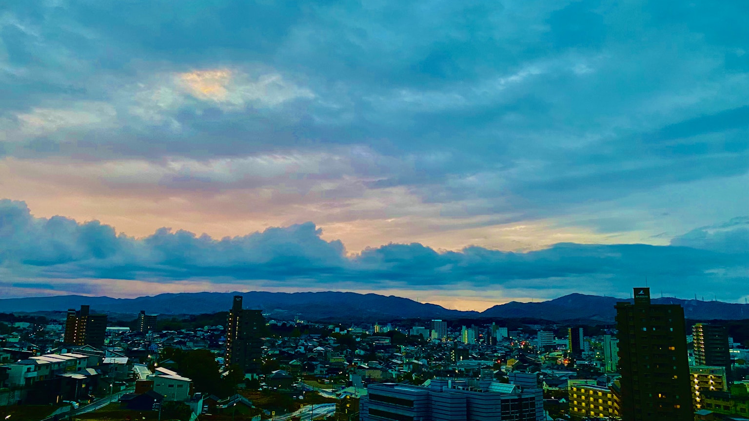 Vue panoramique d'une ville au crépuscule avec des gratte-ciel et des montagnes sous un ciel bleu et orange