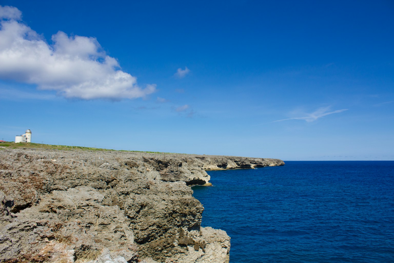 Coastal view with rocky cliffs under a blue sky lighthouse in the distance