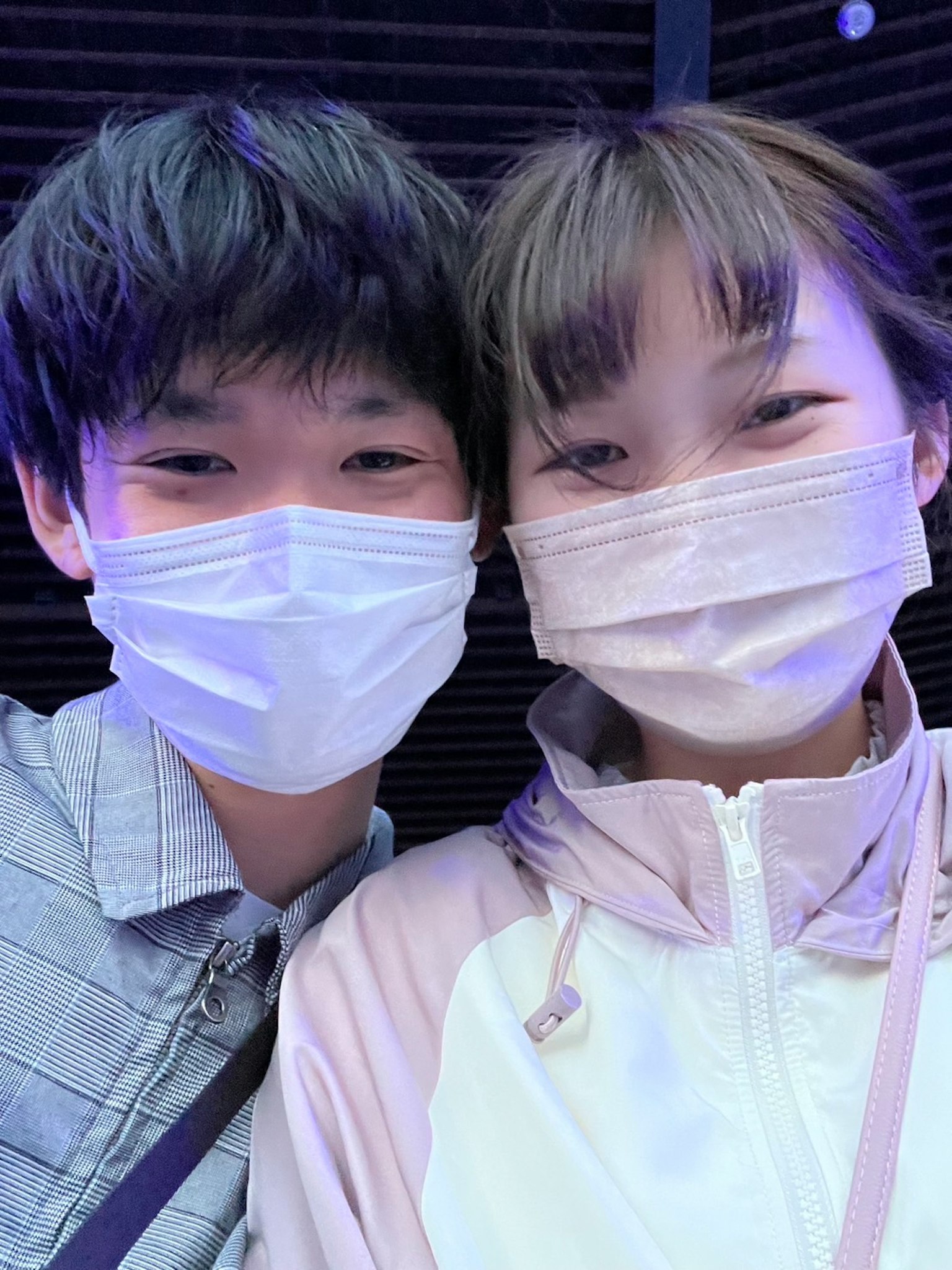 年轻男女佩戴口罩的自拍照，在明亮的灯光下微笑