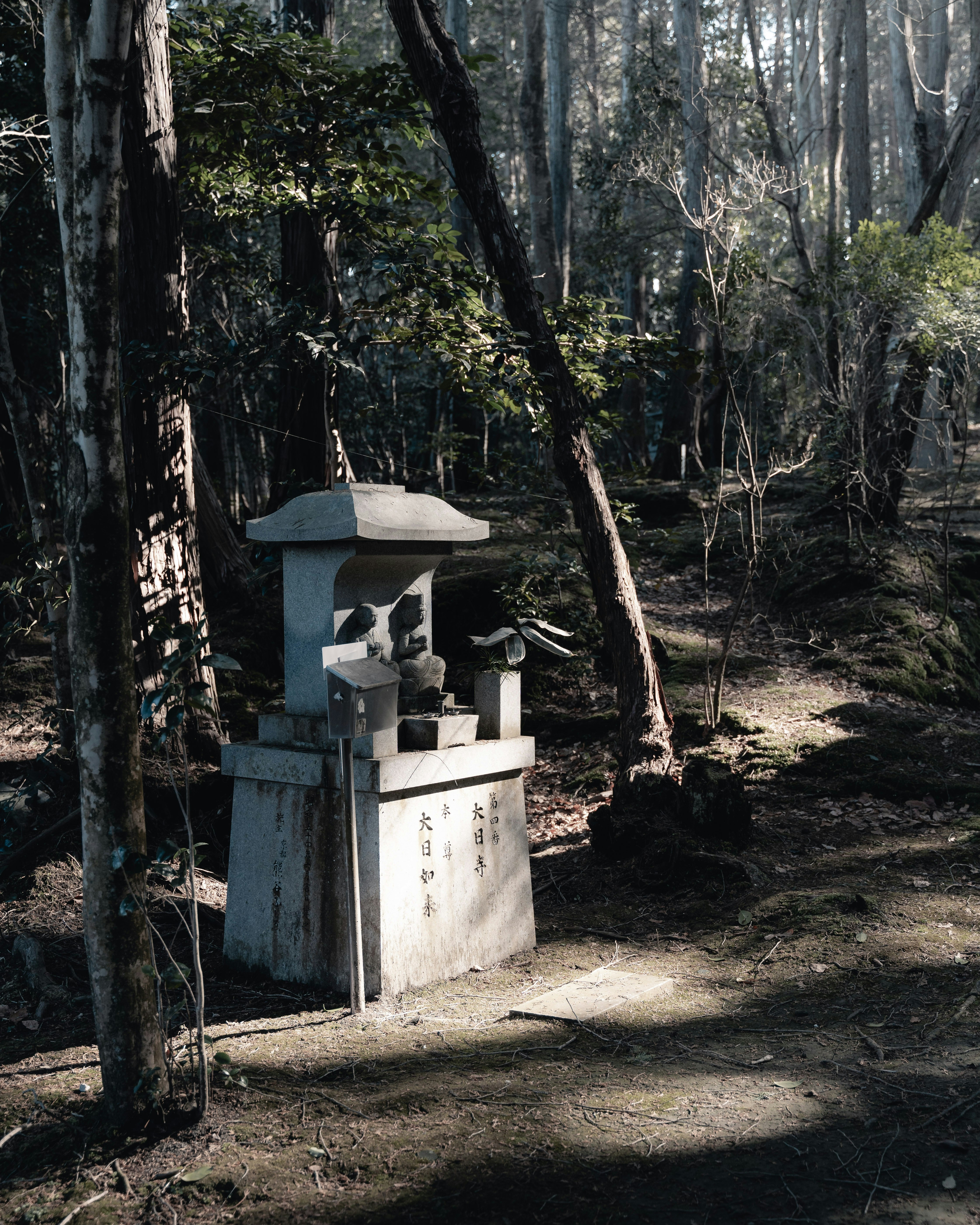森の中に置かれた石の供物台と小さな祠