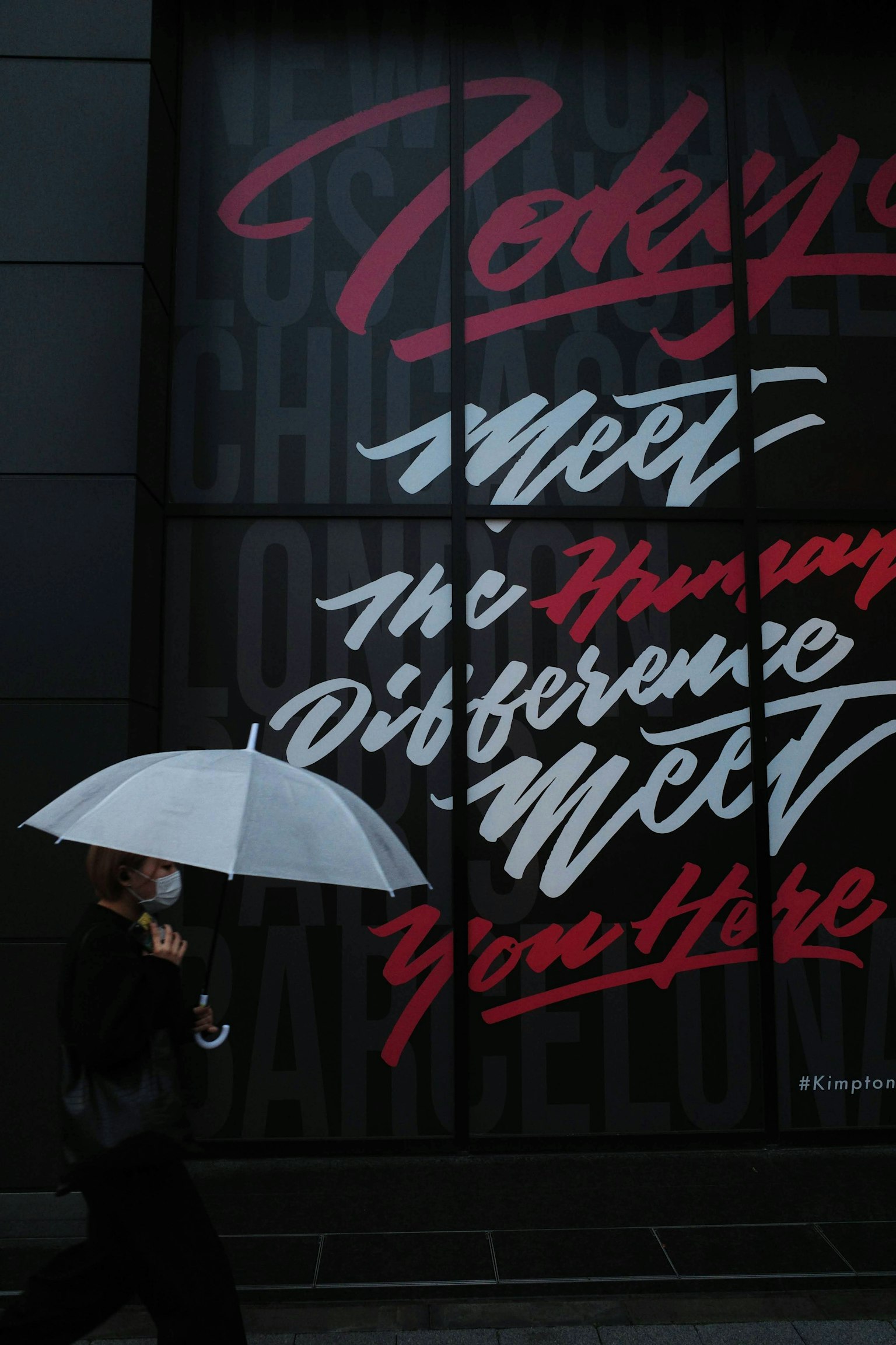 Người đi bộ với chiếc ô trắng trước bức tranh tường đầy màu sắc ở Tokyo