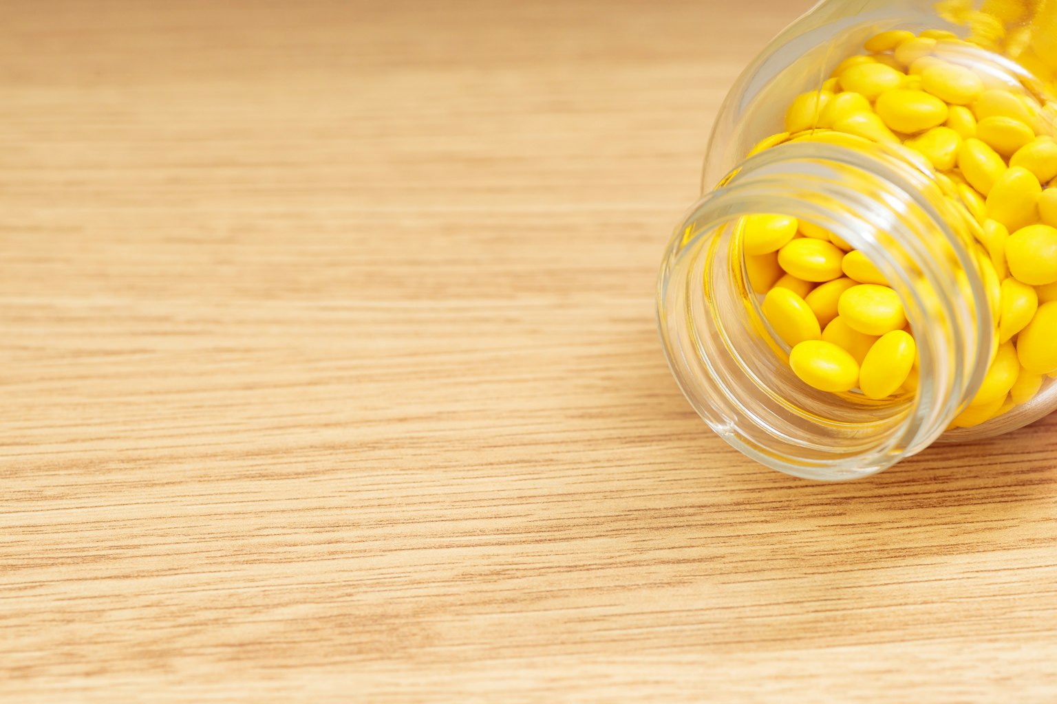 Un frasco de vidrio con pastillas amarillas colocado sobre una mesa de madera