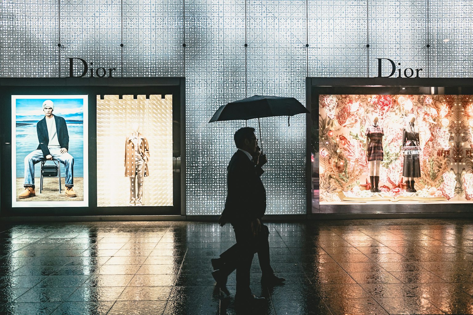 Silhouette di una persona che cammina con un ombrello davanti alle vetrine Dior