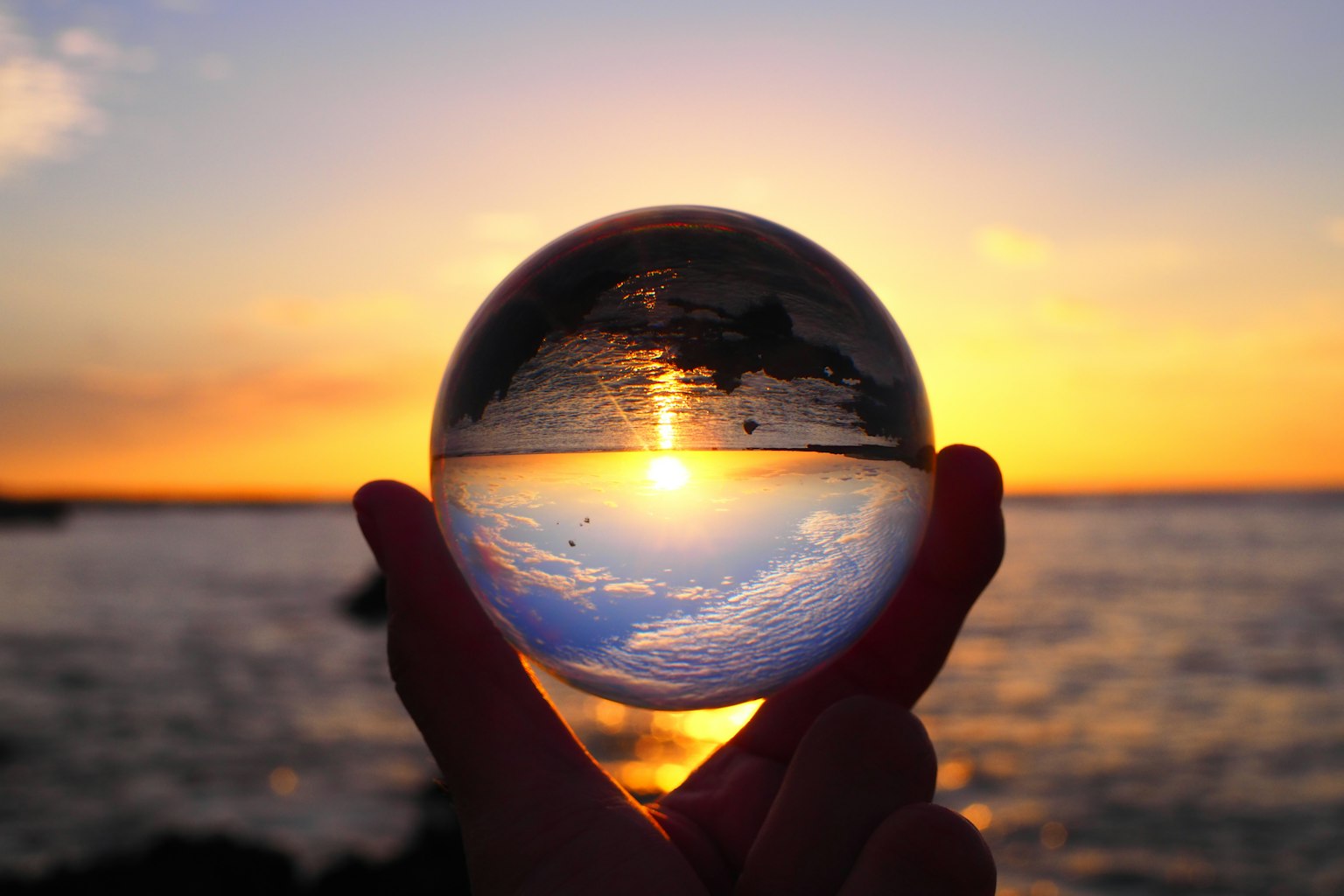 Una bola de cristal sostenida en la mano que refleja una hermosa puesta de sol y vista del océano