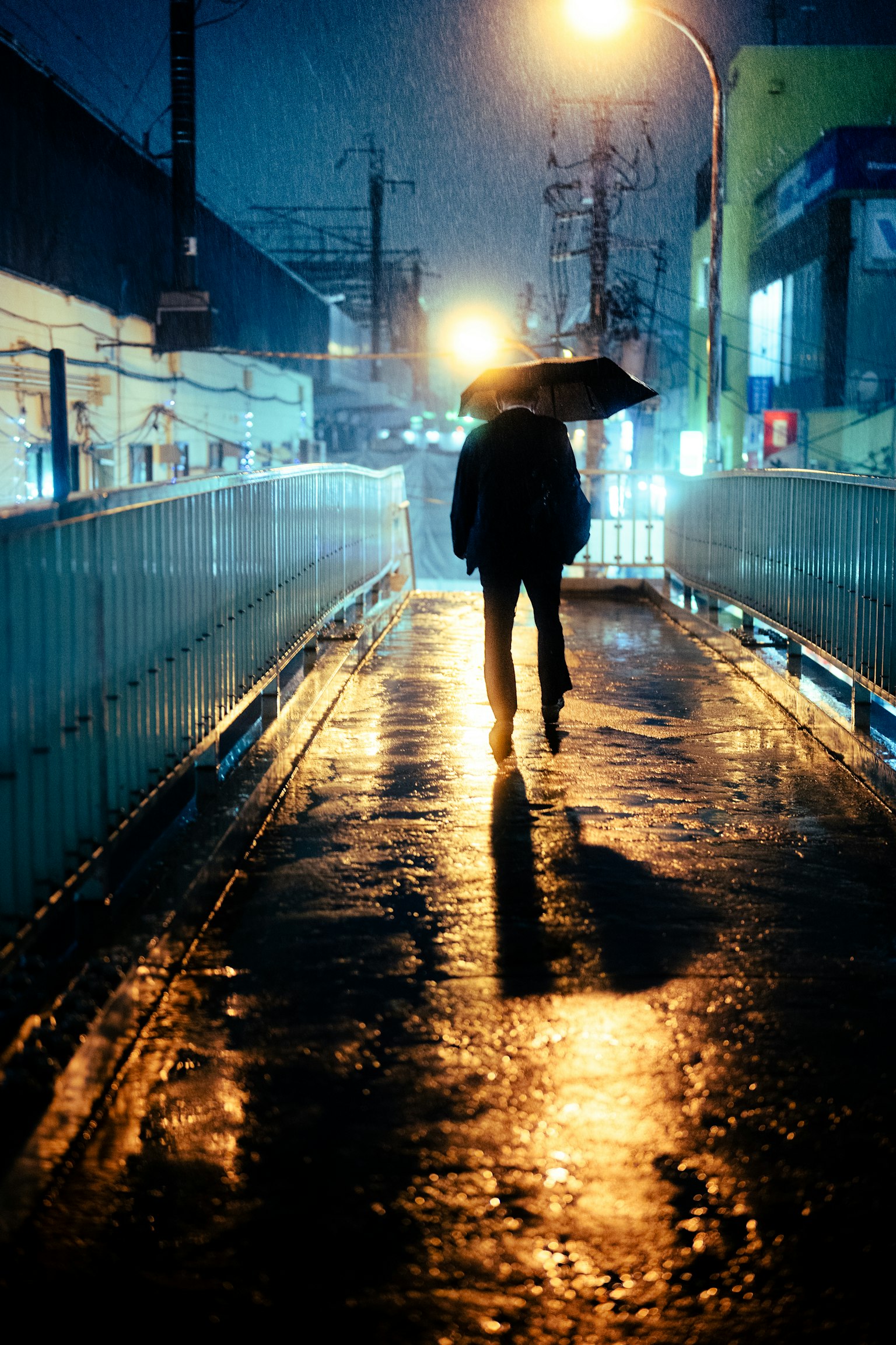 Silhouette of a person walking with an umbrella in the rain street lights reflecting on a wet pavement