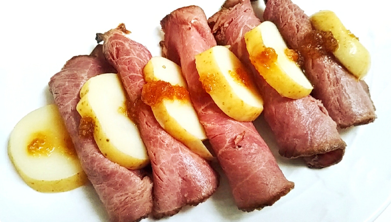 Sliced meat rolls with apple slices arranged on a plate