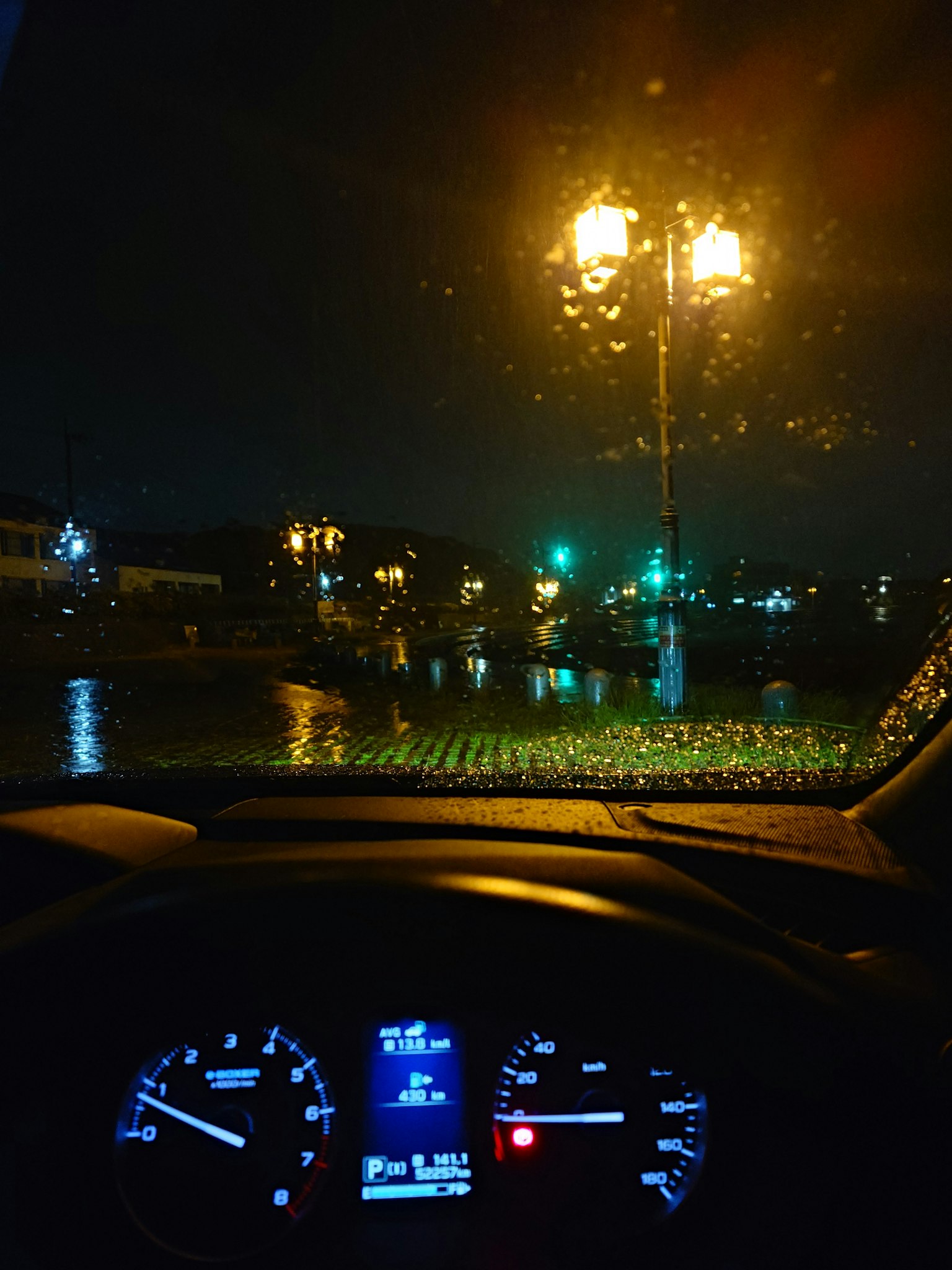 夜晚汽車內部視角，擋風玻璃上有雨水和路燈