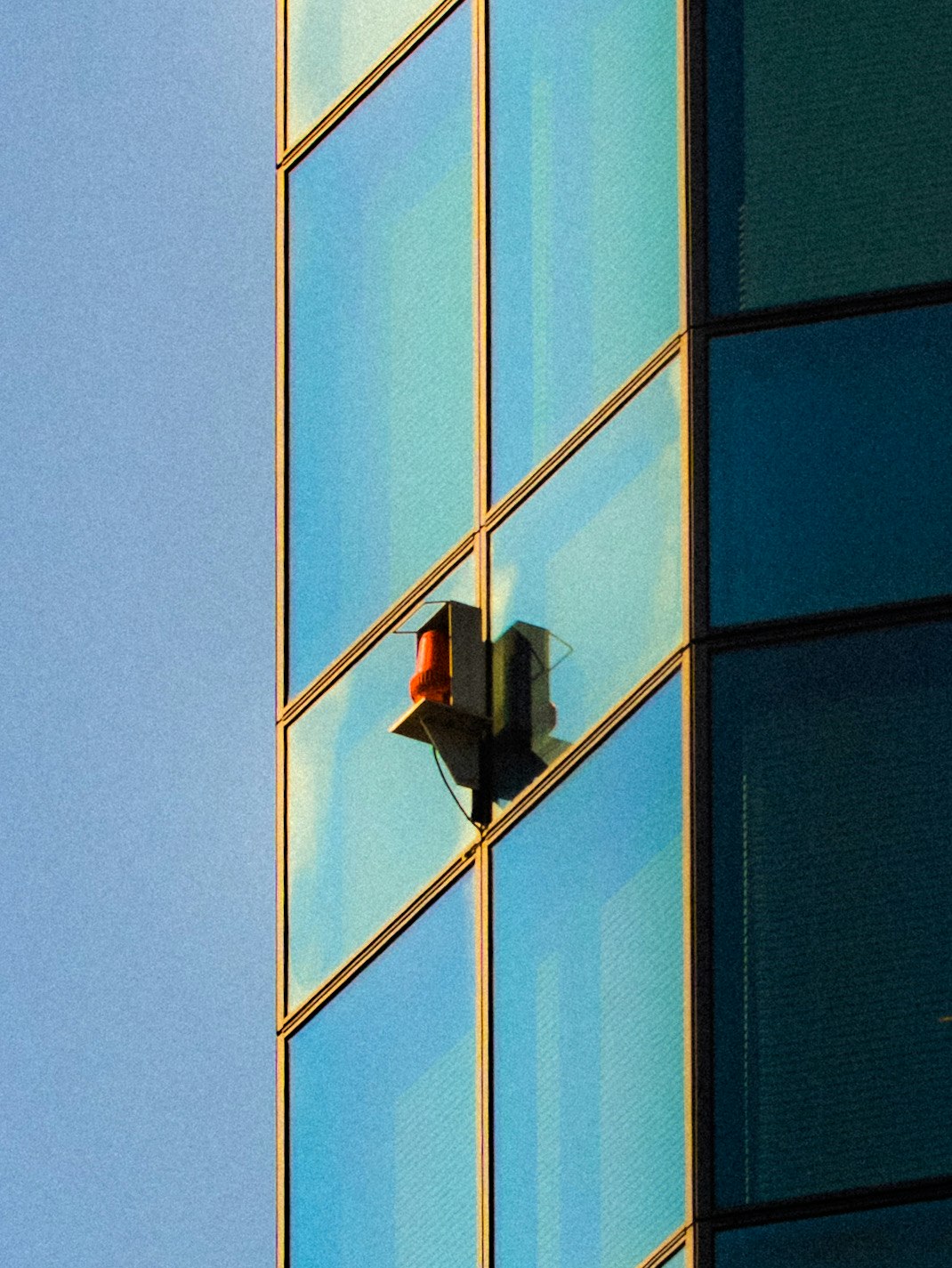 ガラス張りの建物に挟まれた信号機の赤い点滅