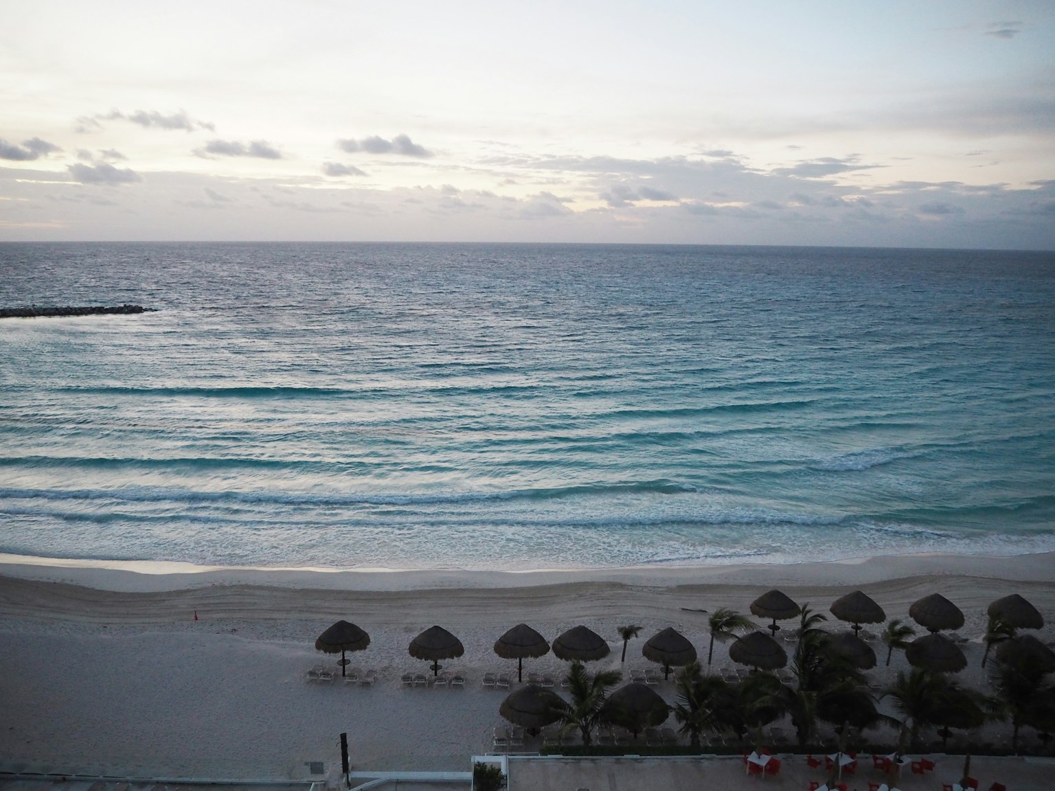 Cảnh bãi biển Cancun với sóng và ghế bãi biển dưới ô rơm