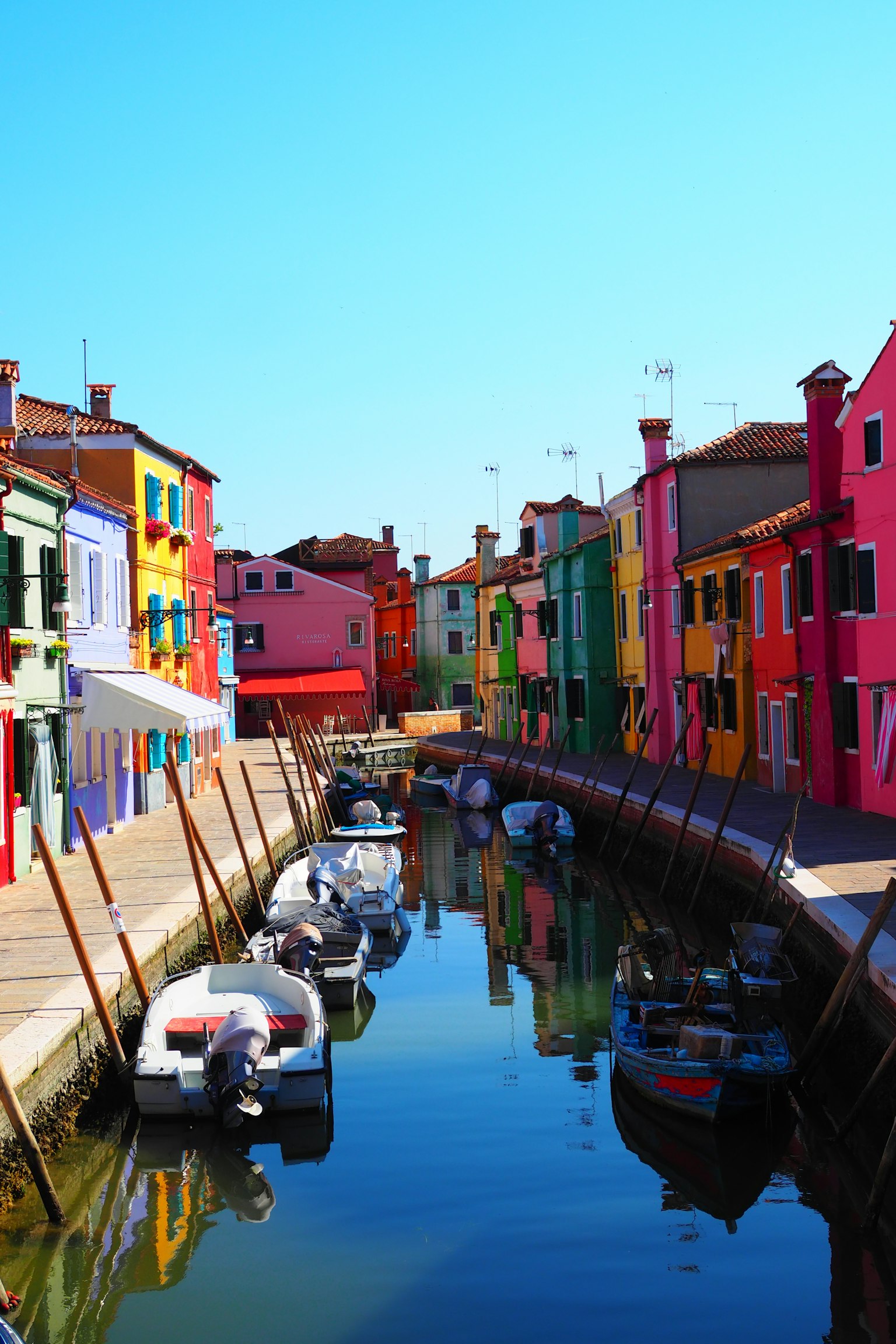 Bunte Gebäude entlang eines Kanals in Burano mit Booten, die sich im Wasser spiegeln