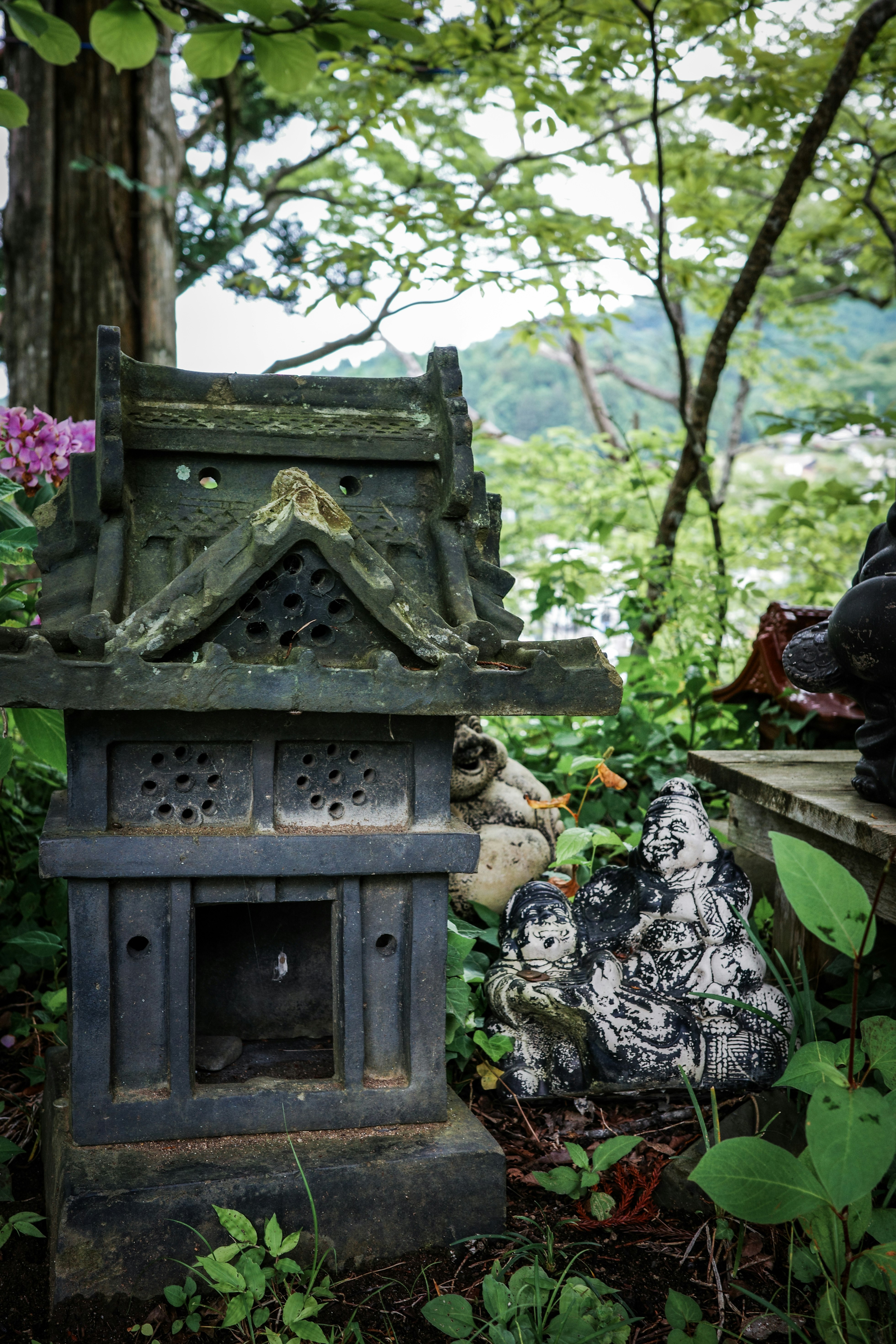 苔むした石の小さな祠と花のある森の小道