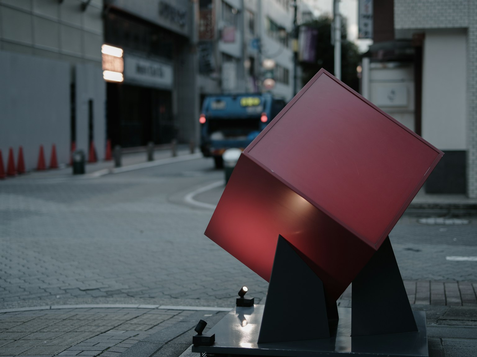 Una scultura a cubo rosso posizionata all'angolo di una strada con un autobus sullo sfondo