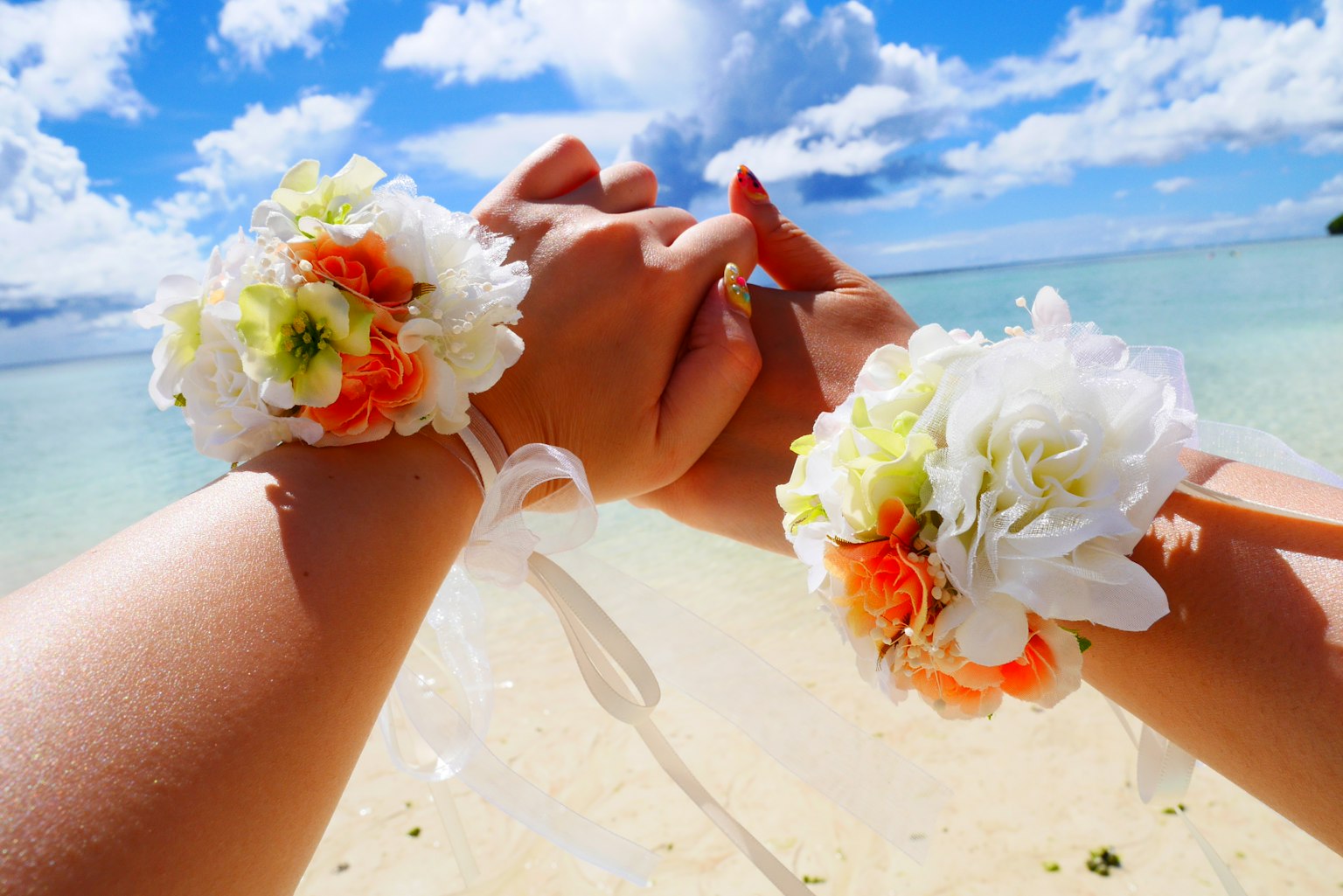 Manos con pulseras de flores y un cielo azul y océano de fondo