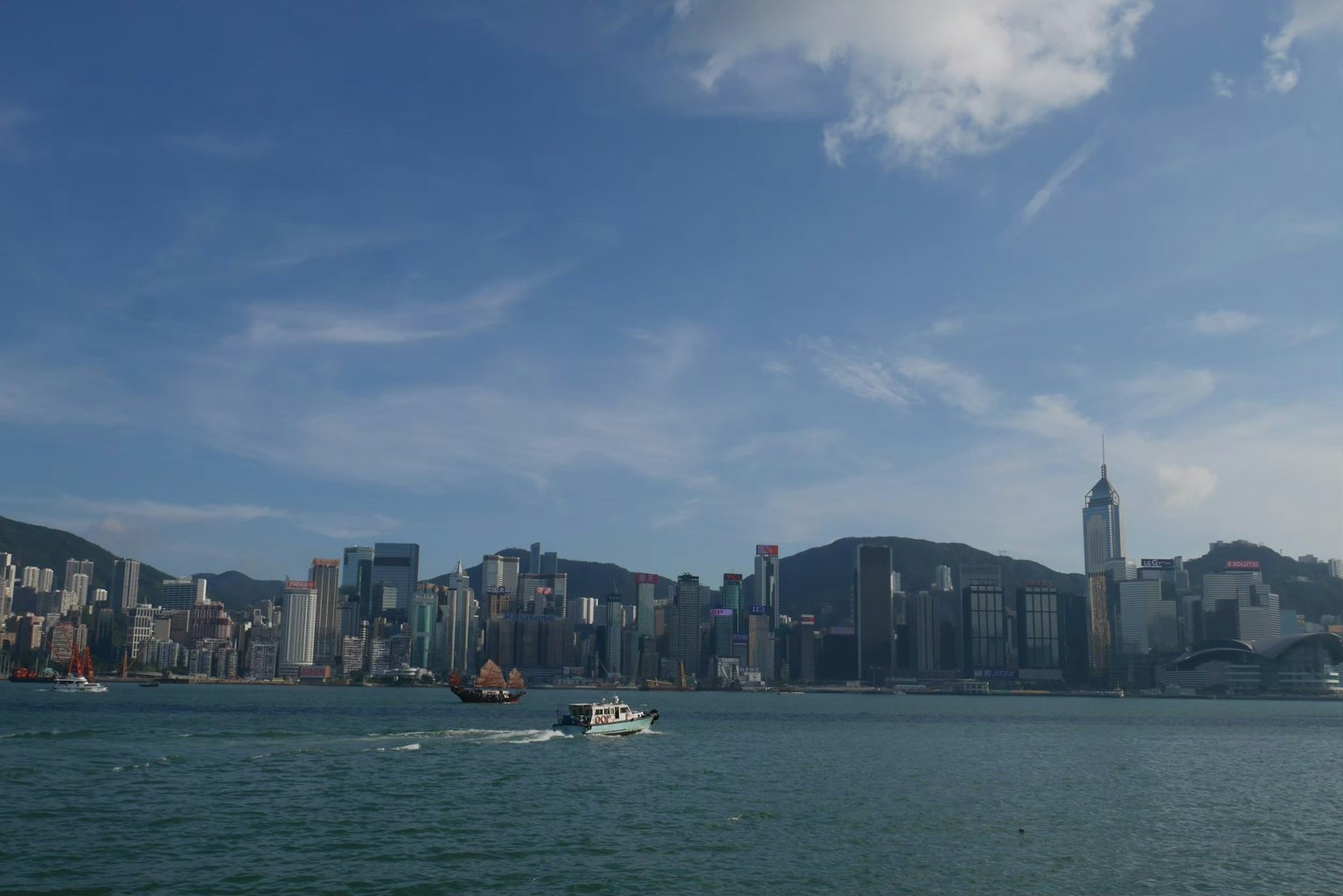 View of Hong Kong skyline with a boat on the water under a blue sky