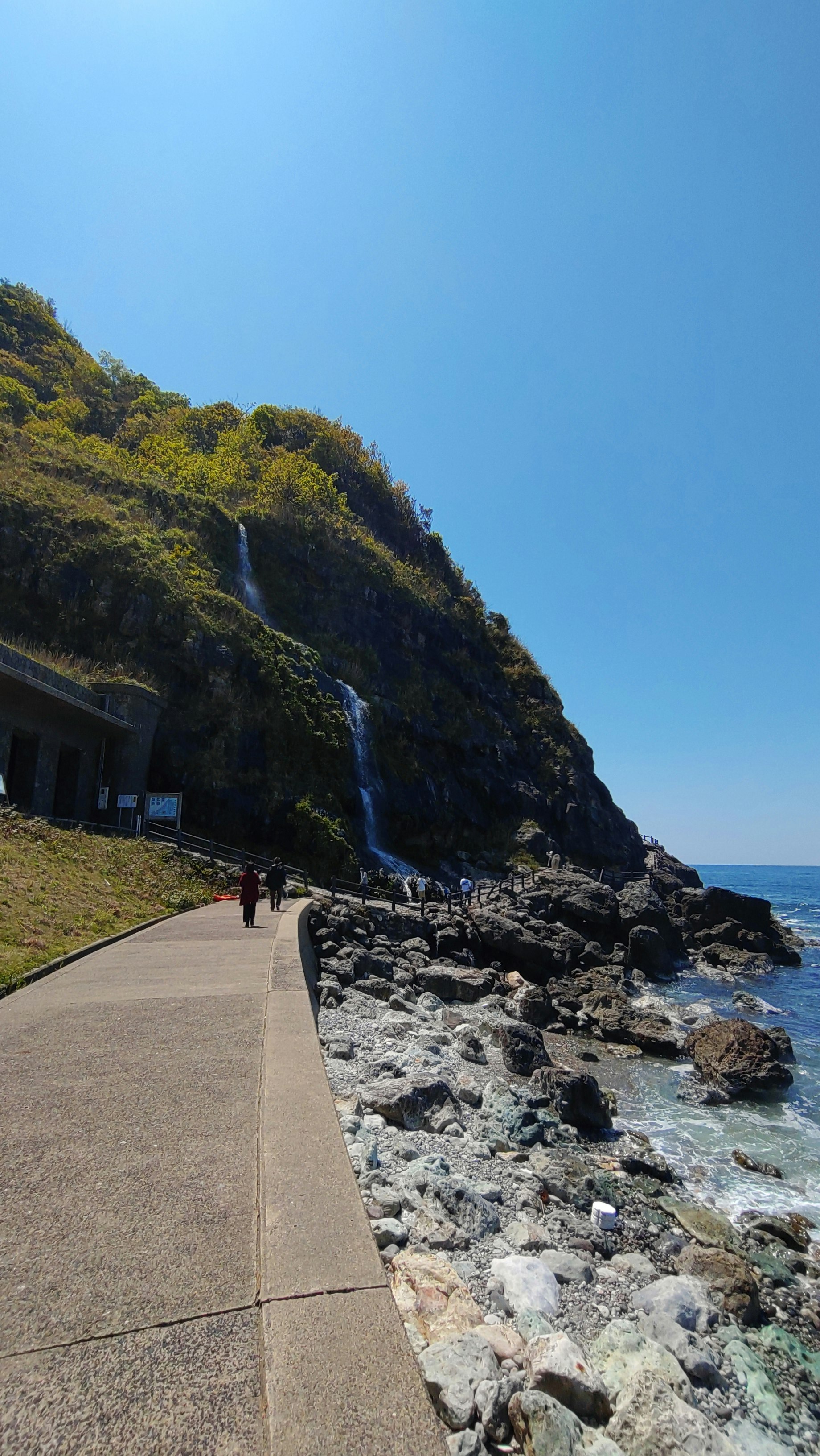 青空の下、海沿いの遊歩道と岩場の景色