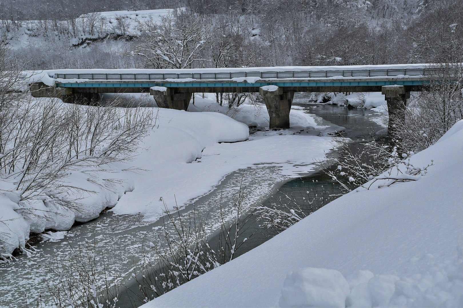 雪の積もる川とコンクリートの橋のある冬の風景