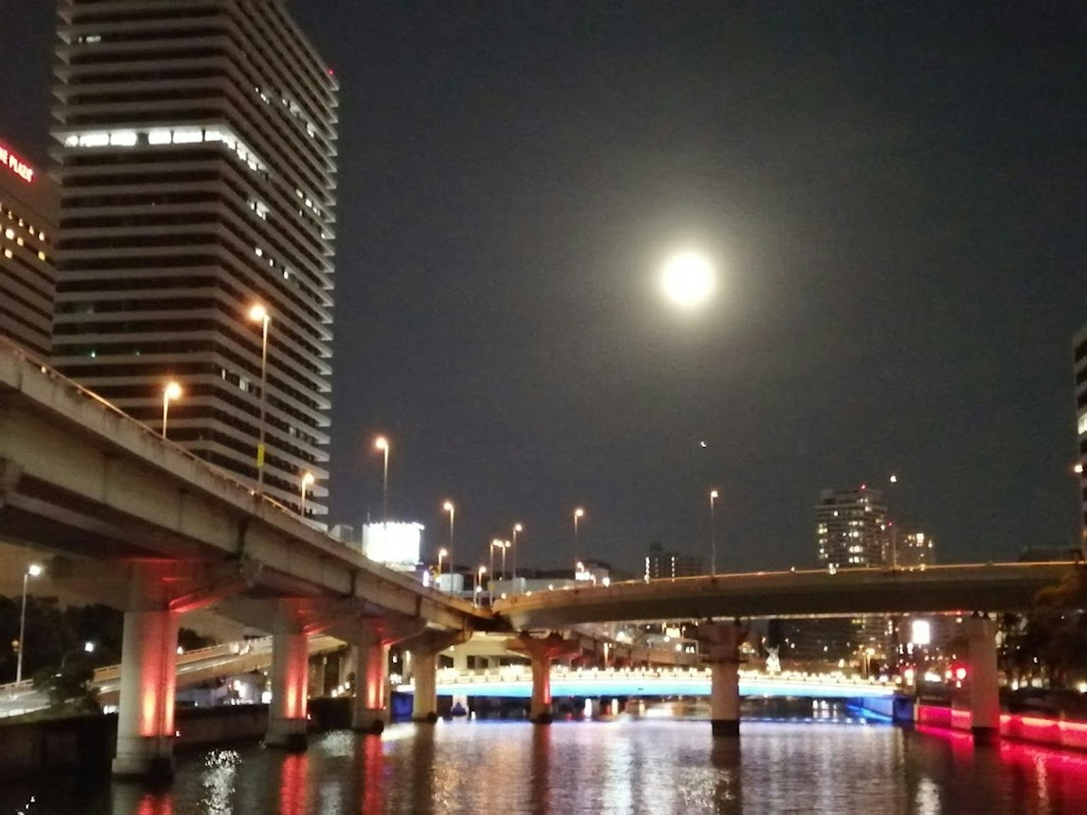 夜晚的河流映照著滿月和燈光閃爍的摩天大樓