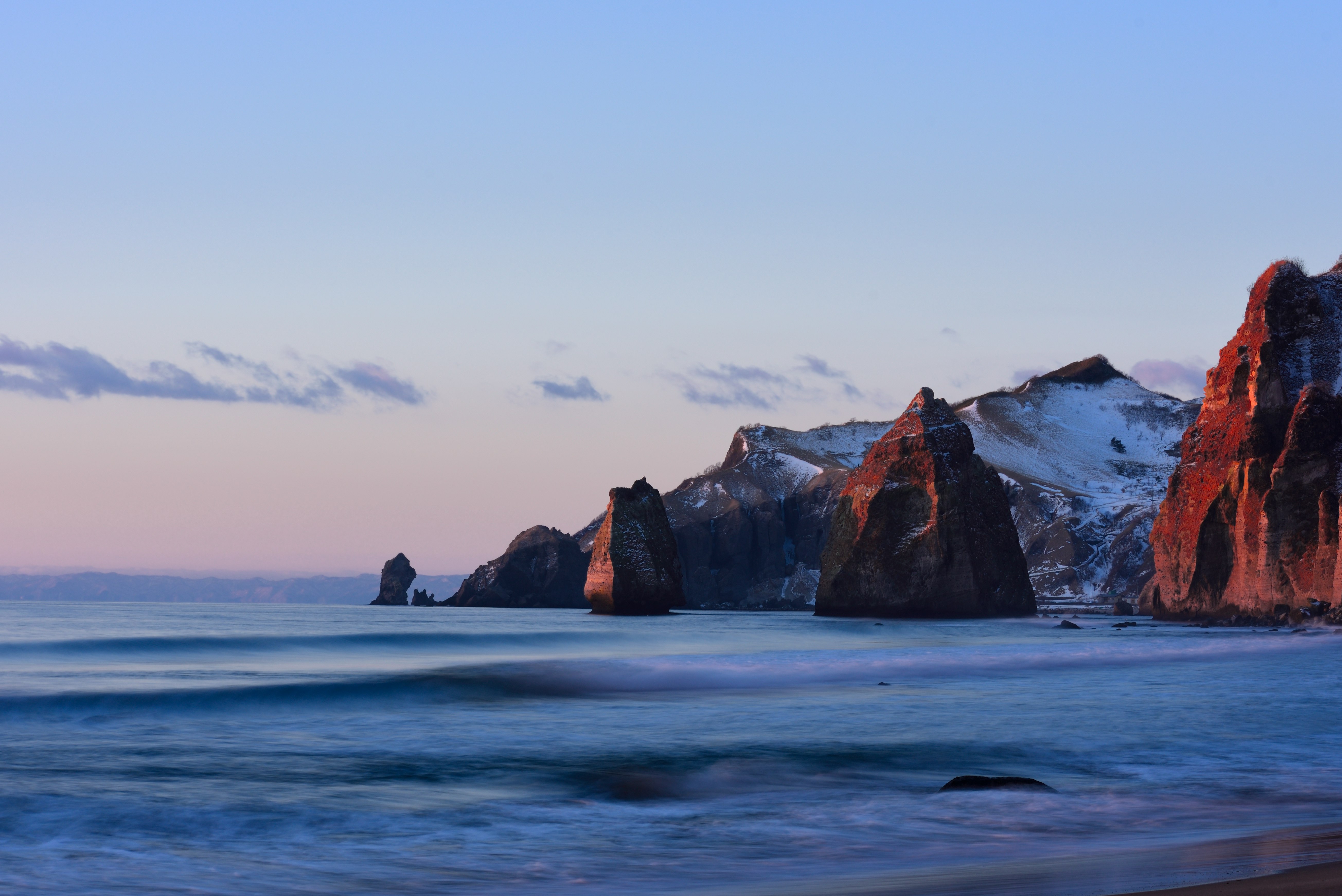 夕暮れの海岸にそびえる岩と波の風景