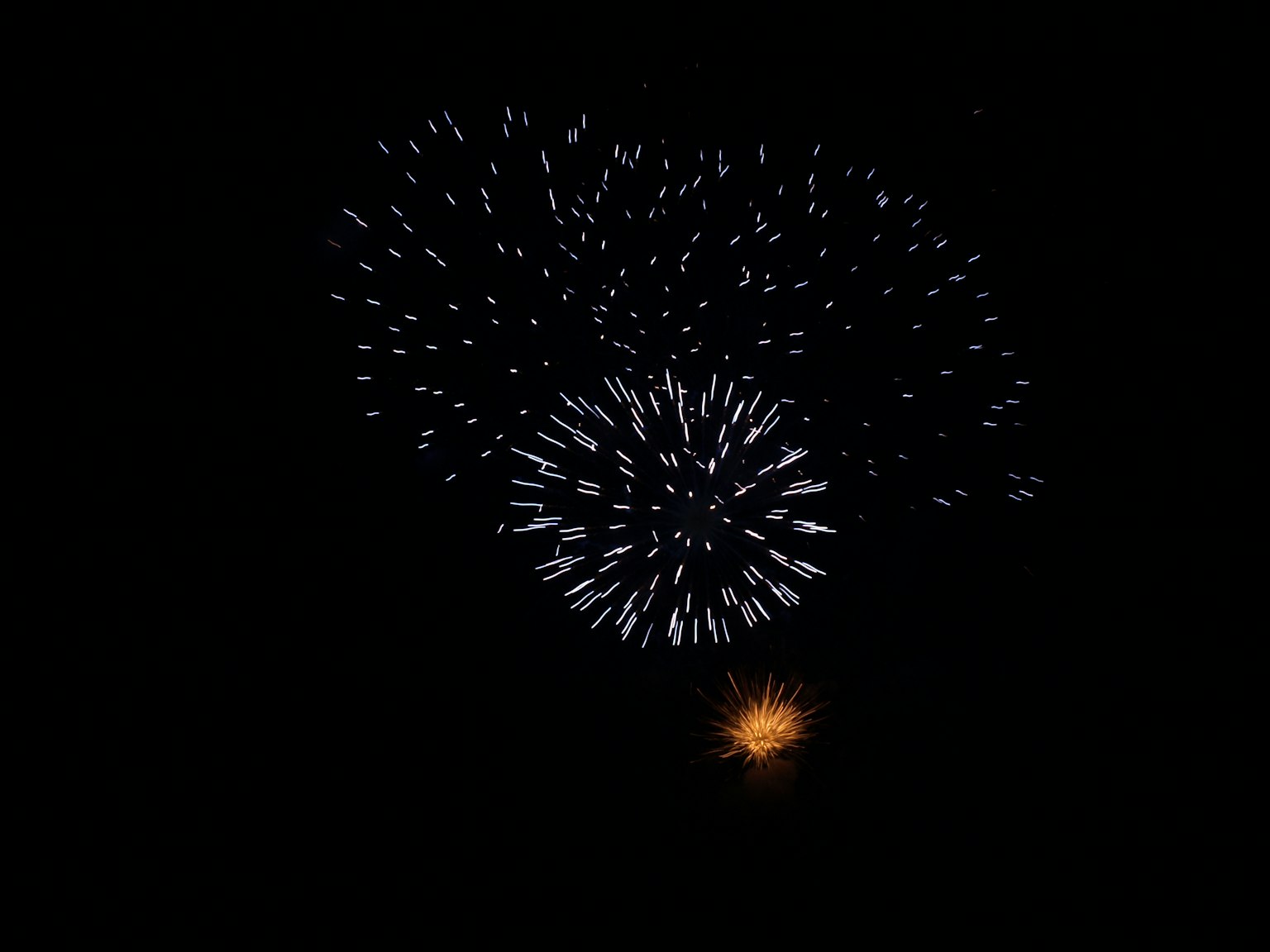 Espectáculo de fuegos artificiales en el cielo nocturno con chispas azules y blancas y un destello naranja abajo