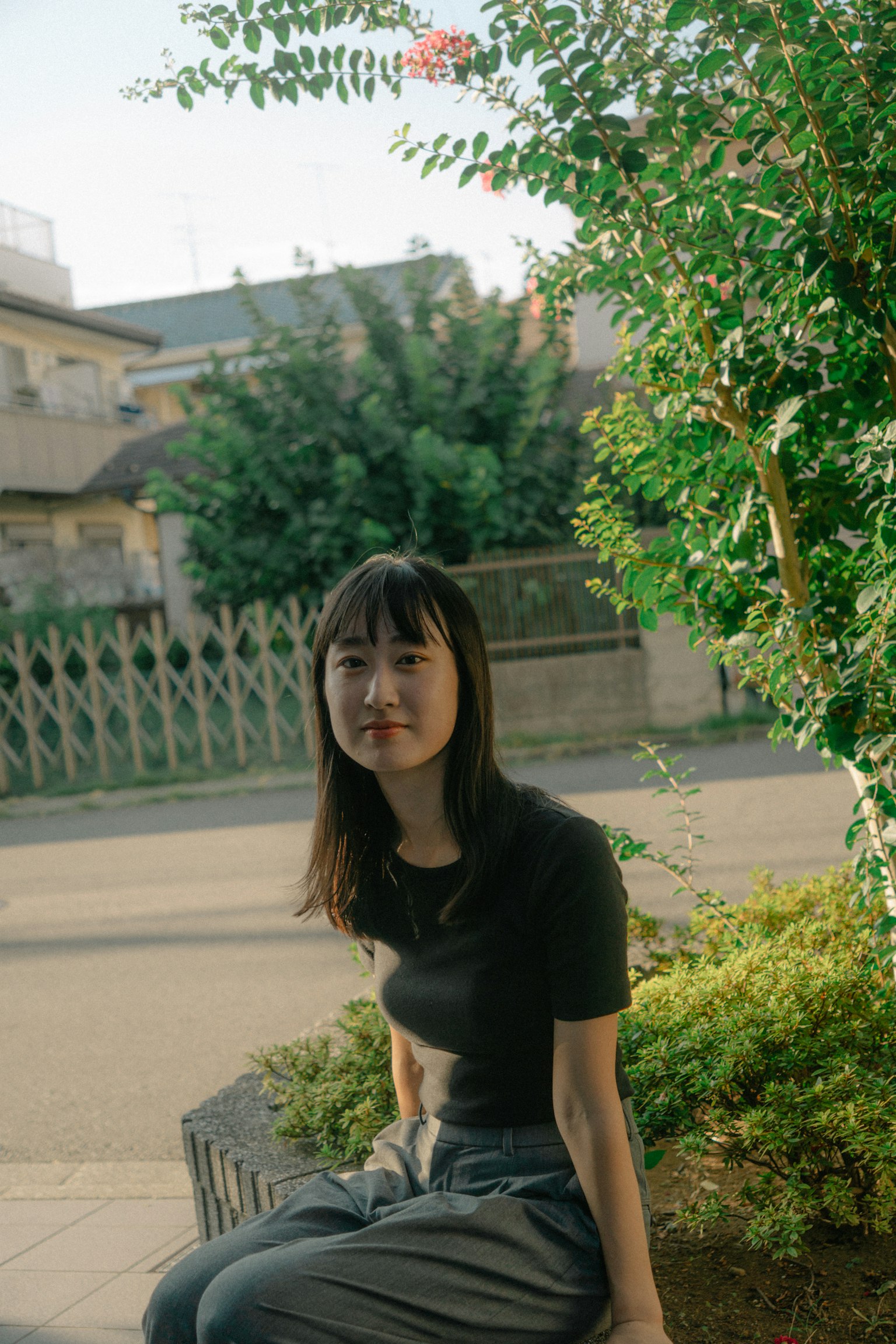 A young woman sitting near green plants in a casual outfit